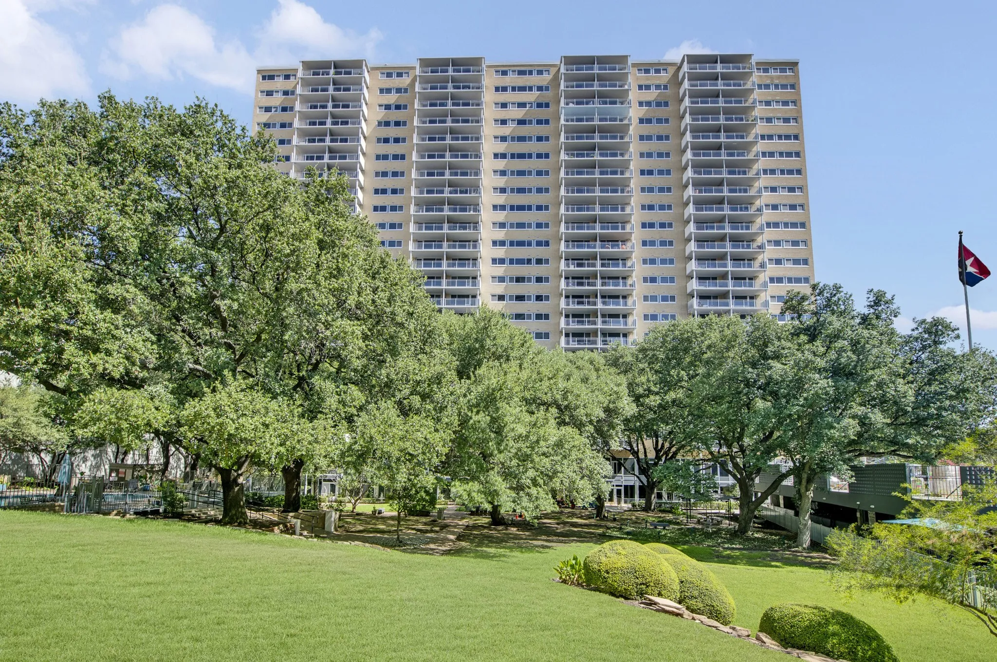 High-rise architecture with numerous balconies, set against a backdrop of mature trees and manicured lawns