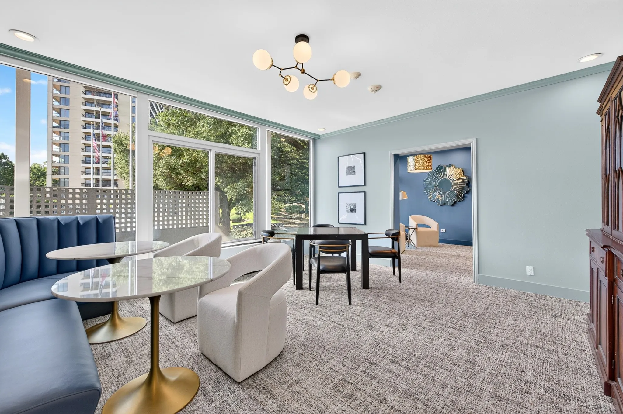 Expansive window wall, contemporary lighting fixture, light blue wall paint, wood-finish built-in cabinetry, and patterned carpeting