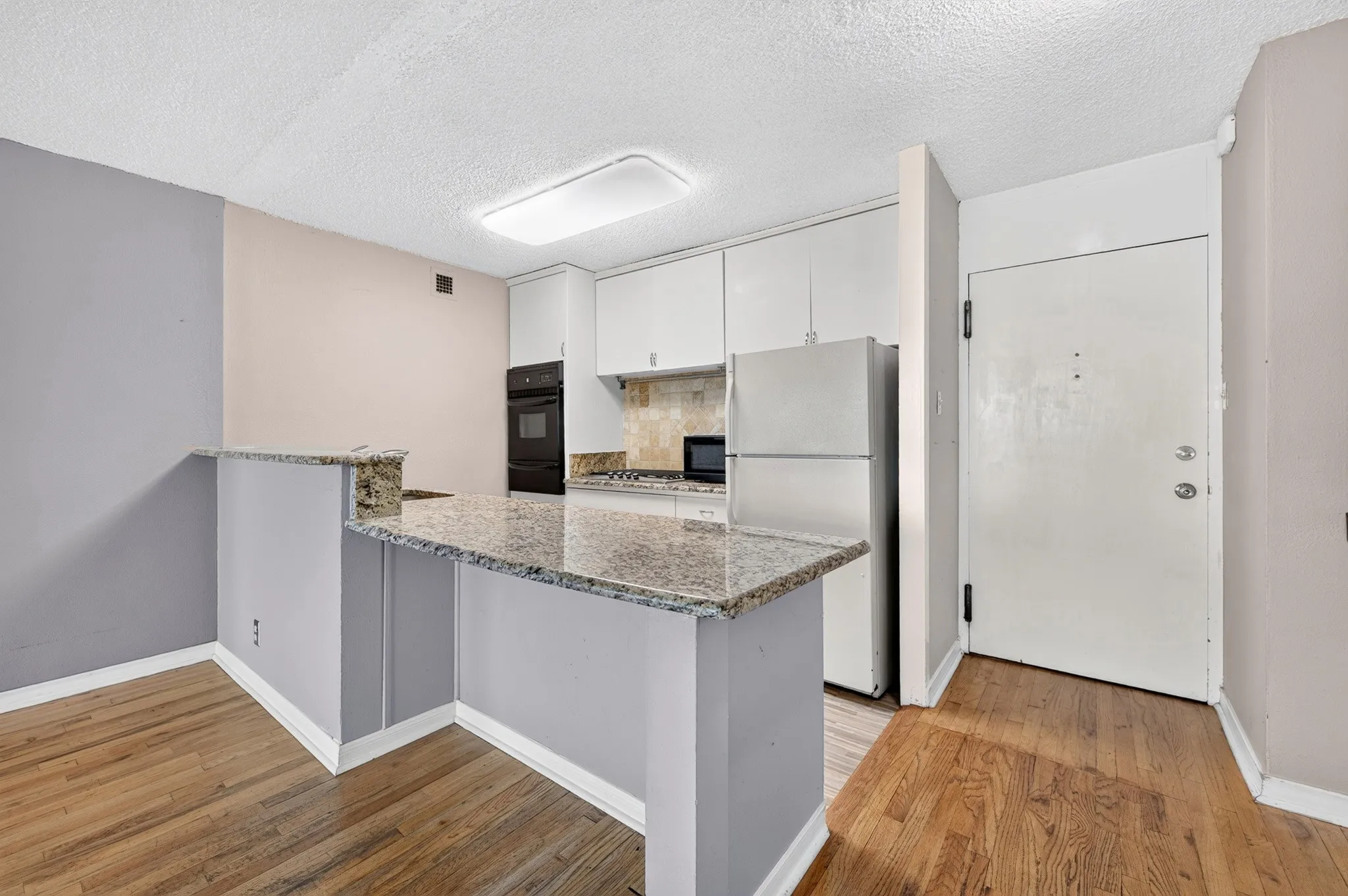 Kitchen with light wood flooring, granite countertops, white cabinetry, and stainless steel appliances