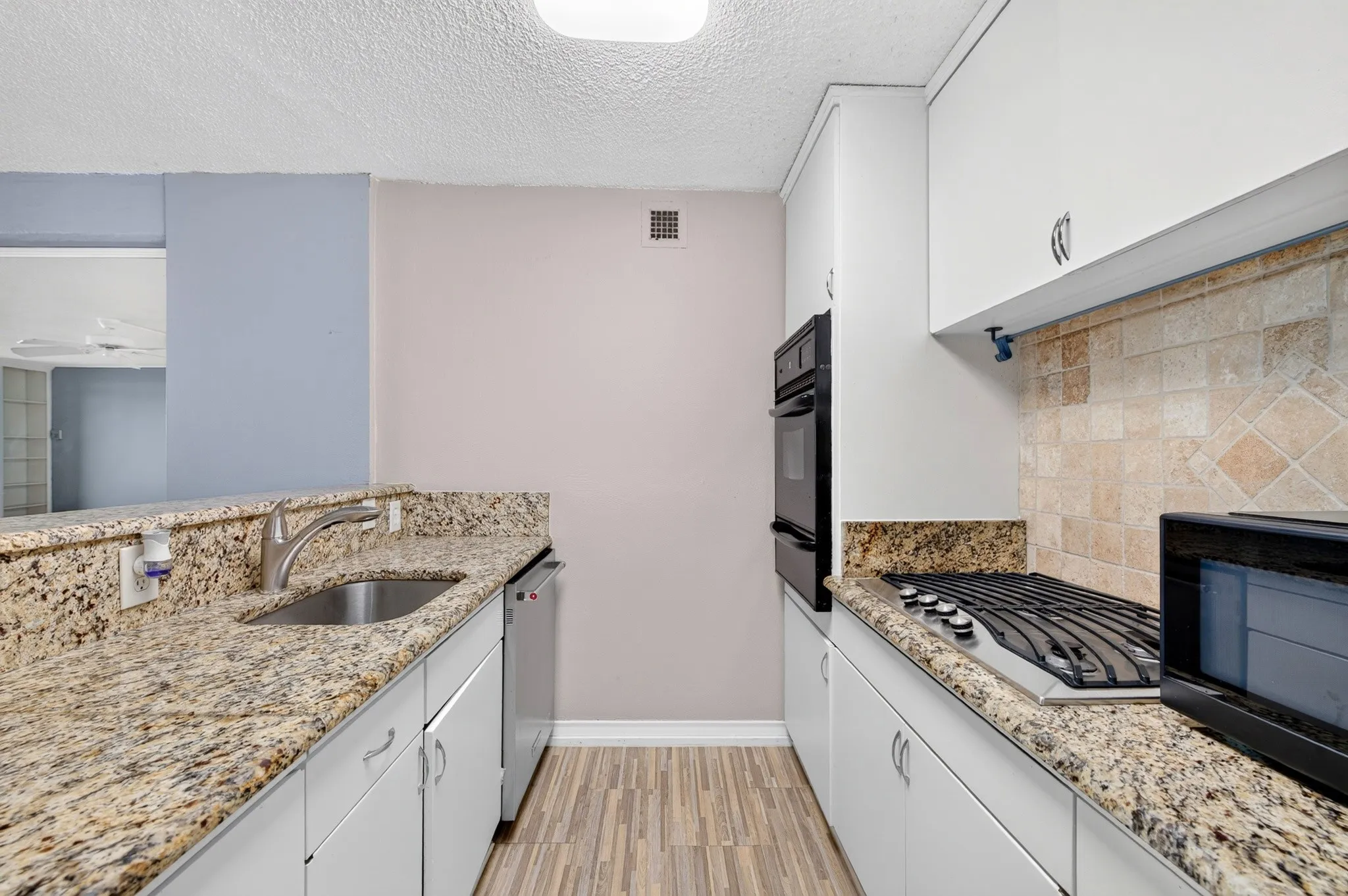 Galley kitchen featuring granite countertops, wood-finish flooring, white cabinetry with silver hardware, a stainless steel sink, and a built-in double oven
