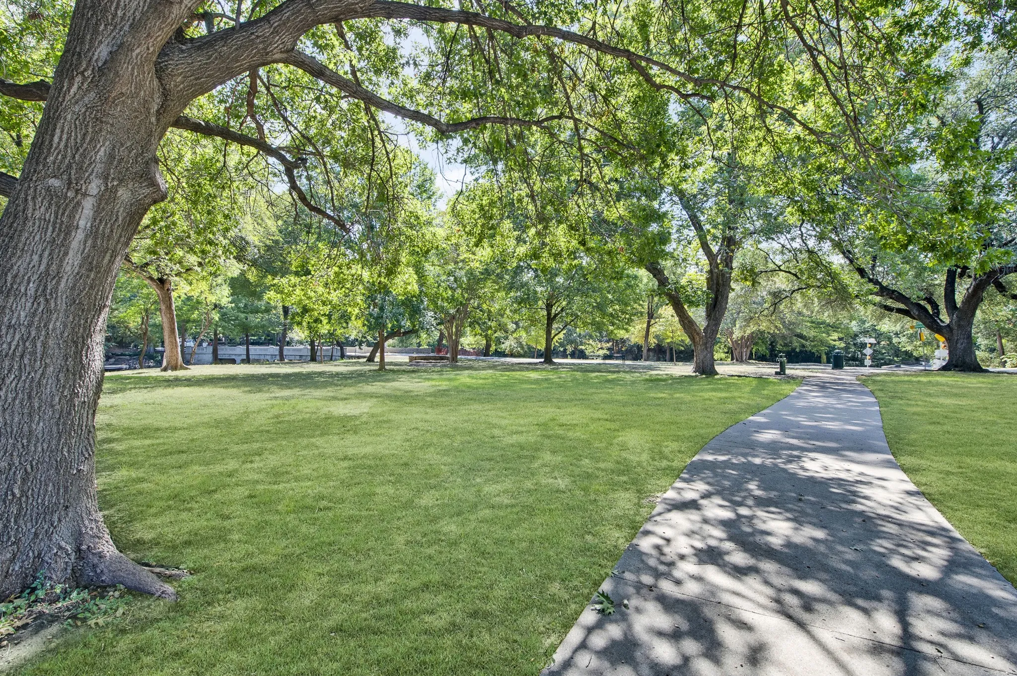 Expansive park setting featuring mature trees, a curving paved pathway, and lush green lawn