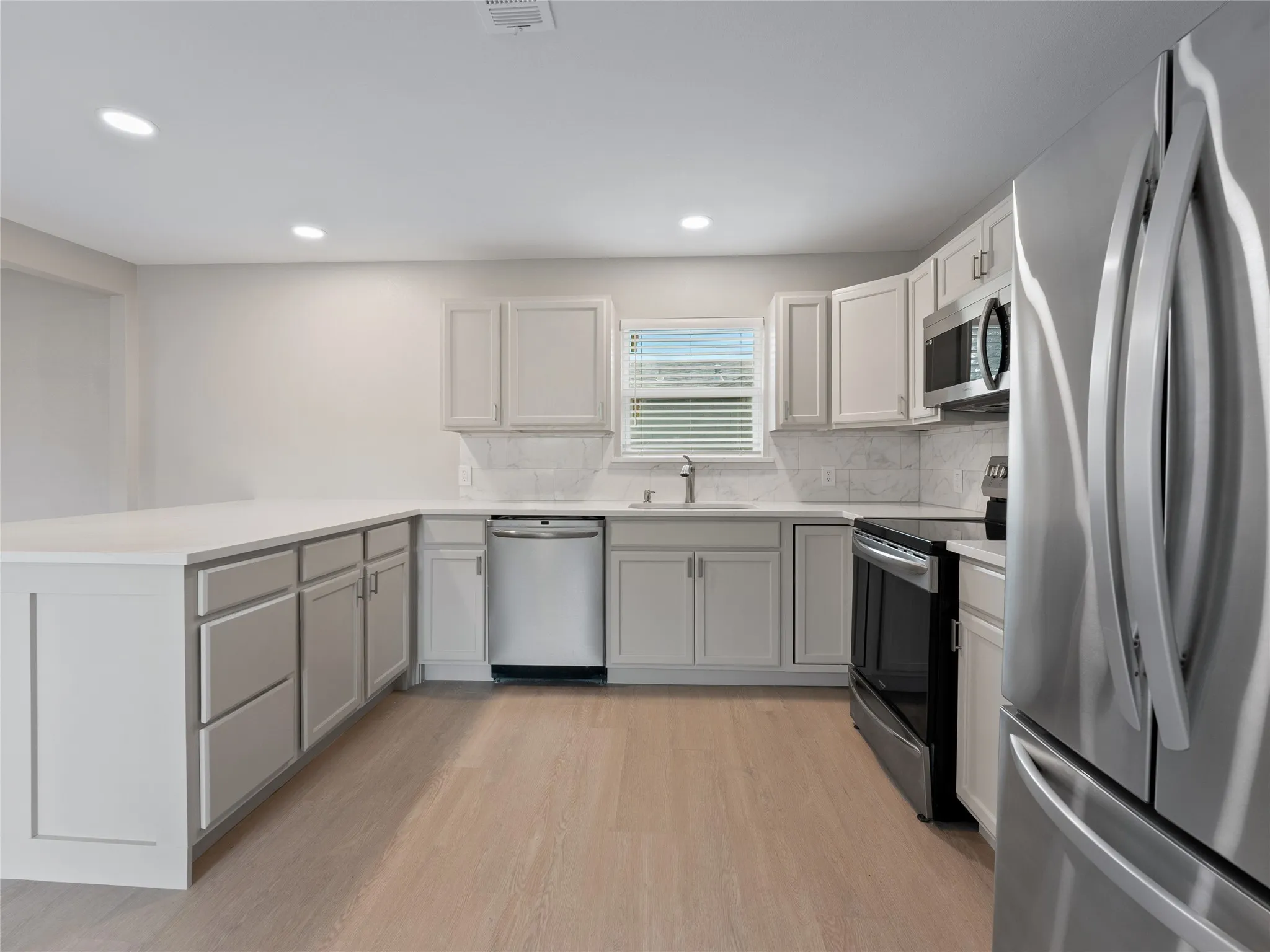 Kitchen featuring light wood-finish flooring, white cabinetry, integrated stainless steel appliances, white countertop, and a white tile backsplash
