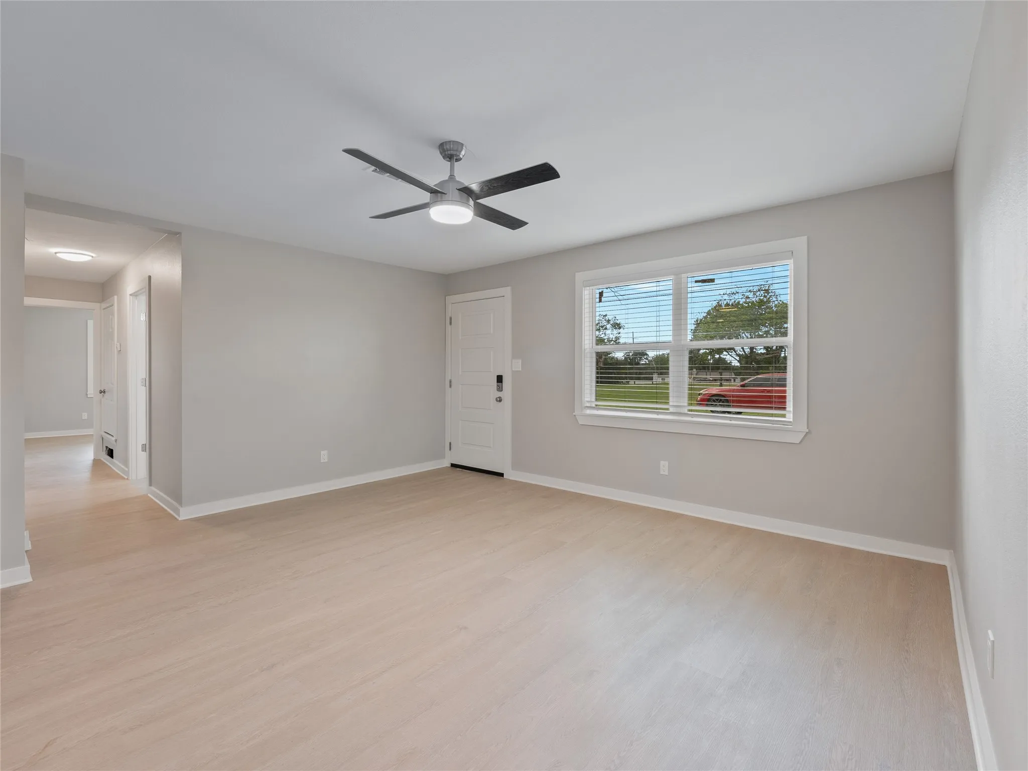 Light wood-finish flooring, a white paneled entry door, a ceiling fan with integrated lighting, and a window with horizontal blinds