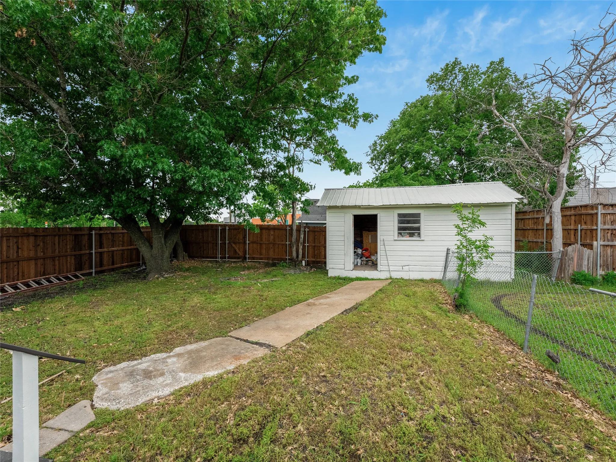 Expansive backyard with a storage shed, concrete pathway, chain-link fence, and a wooden privacy fence