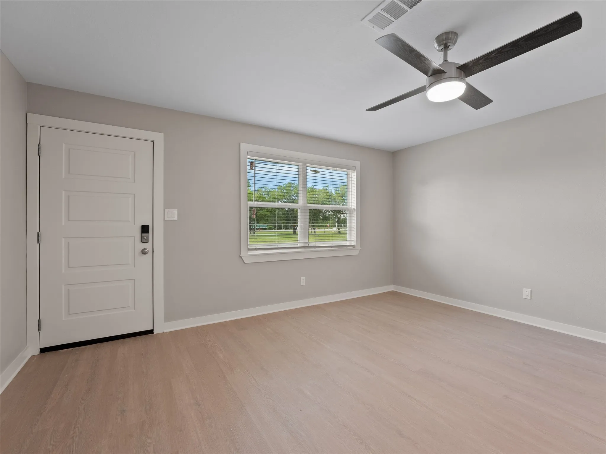 Wood-finish flooring, white panel door with smart lock, window with blinds, and ceiling fan with integrated lighting