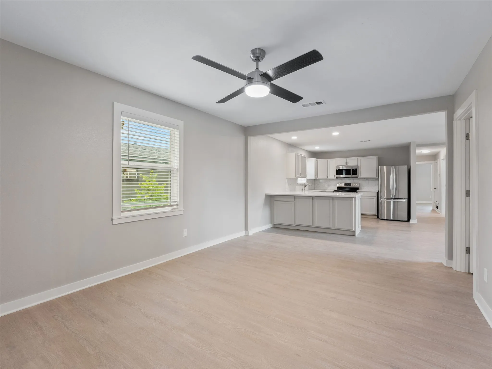 Open-concept living area featuring wood-finish flooring, a contemporary ceiling fan, and a kitchen with stainless steel appliances, light cabinetry, and a breakfast bar