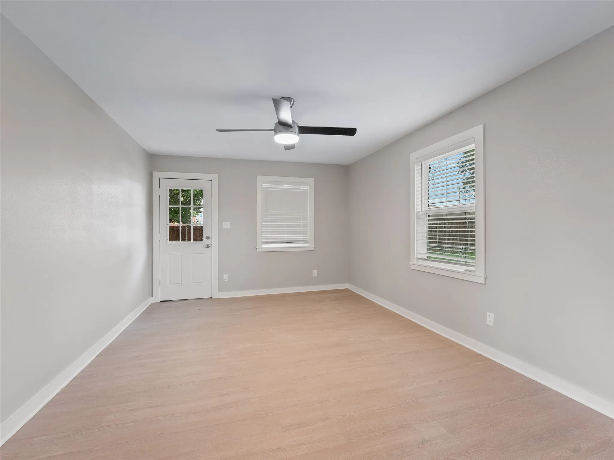 Spacious room featuring wood-finish flooring, light gray wall tones, a ceiling fan, and a glass-paneled door