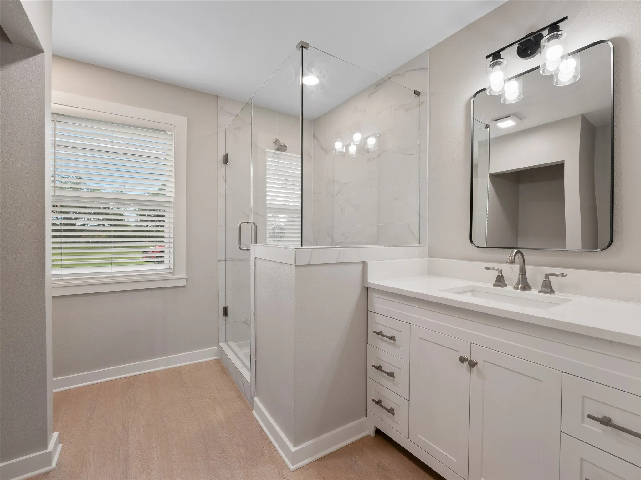 White vanity with a single basin sink and brushed nickel faucet, large wall mirror with black trim, and a three-light vanity fixture