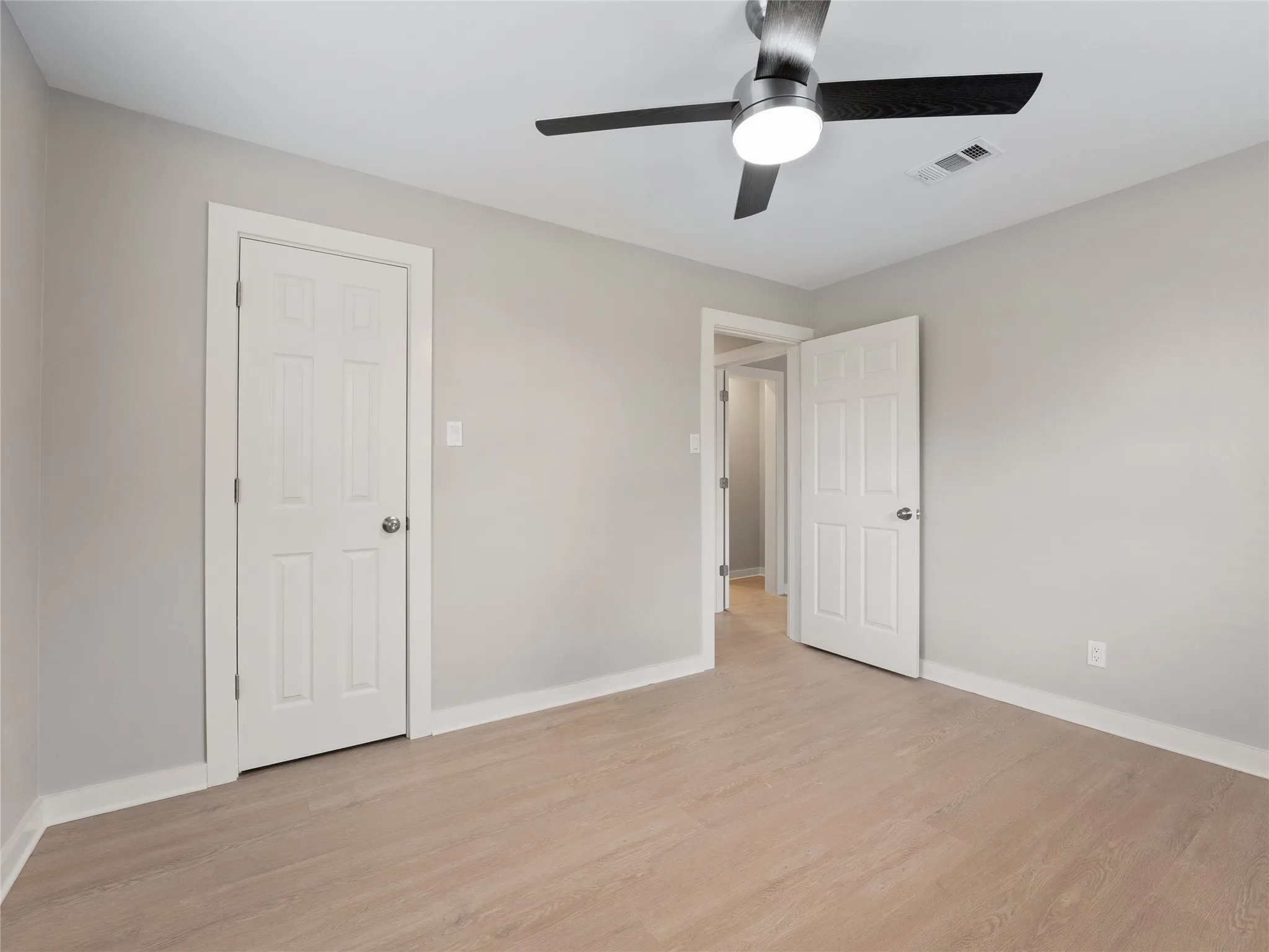 Light wood-finish flooring, neutral wall tones, and a contemporary ceiling fan with integrated lighting
