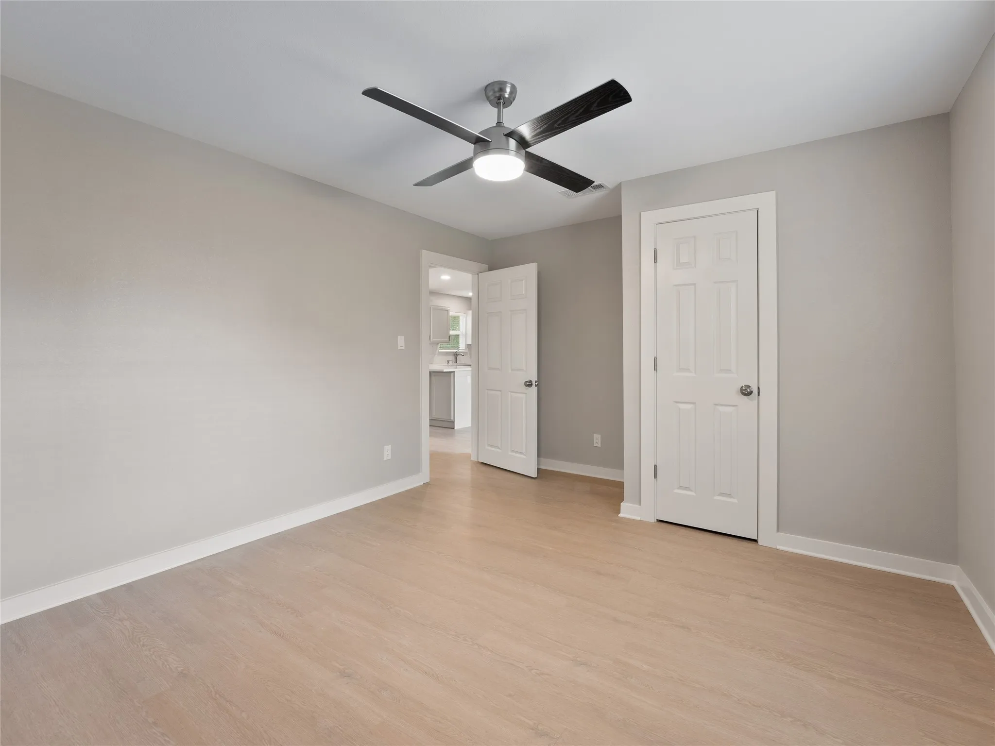 Wood-finish flooring, neutral wall tones, modern ceiling fan, white paneled doors, and white trim