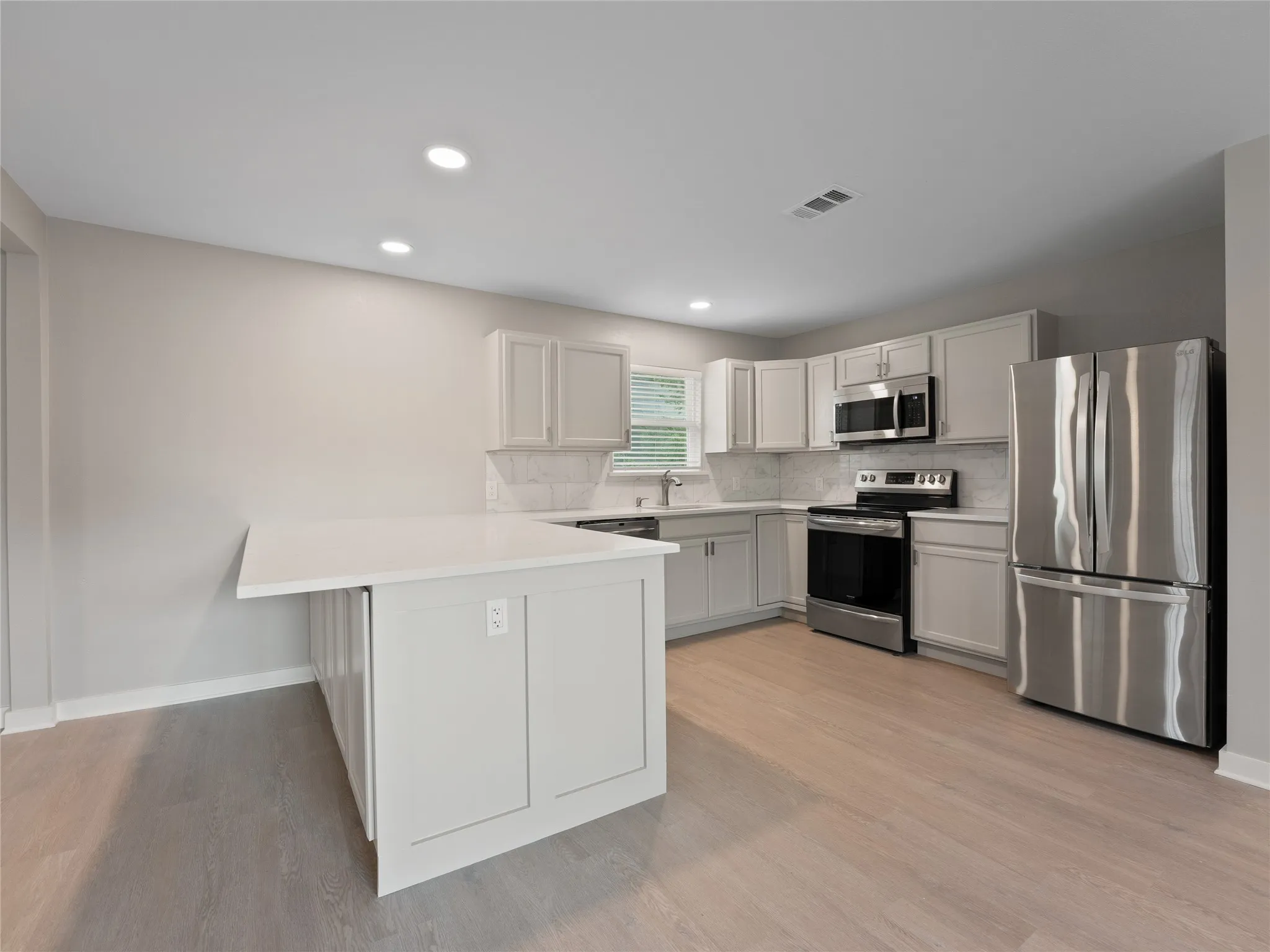 Kitchen featuring a white island with countertop seating, light wood-finish flooring, recessed lighting, and stainless steel appliances