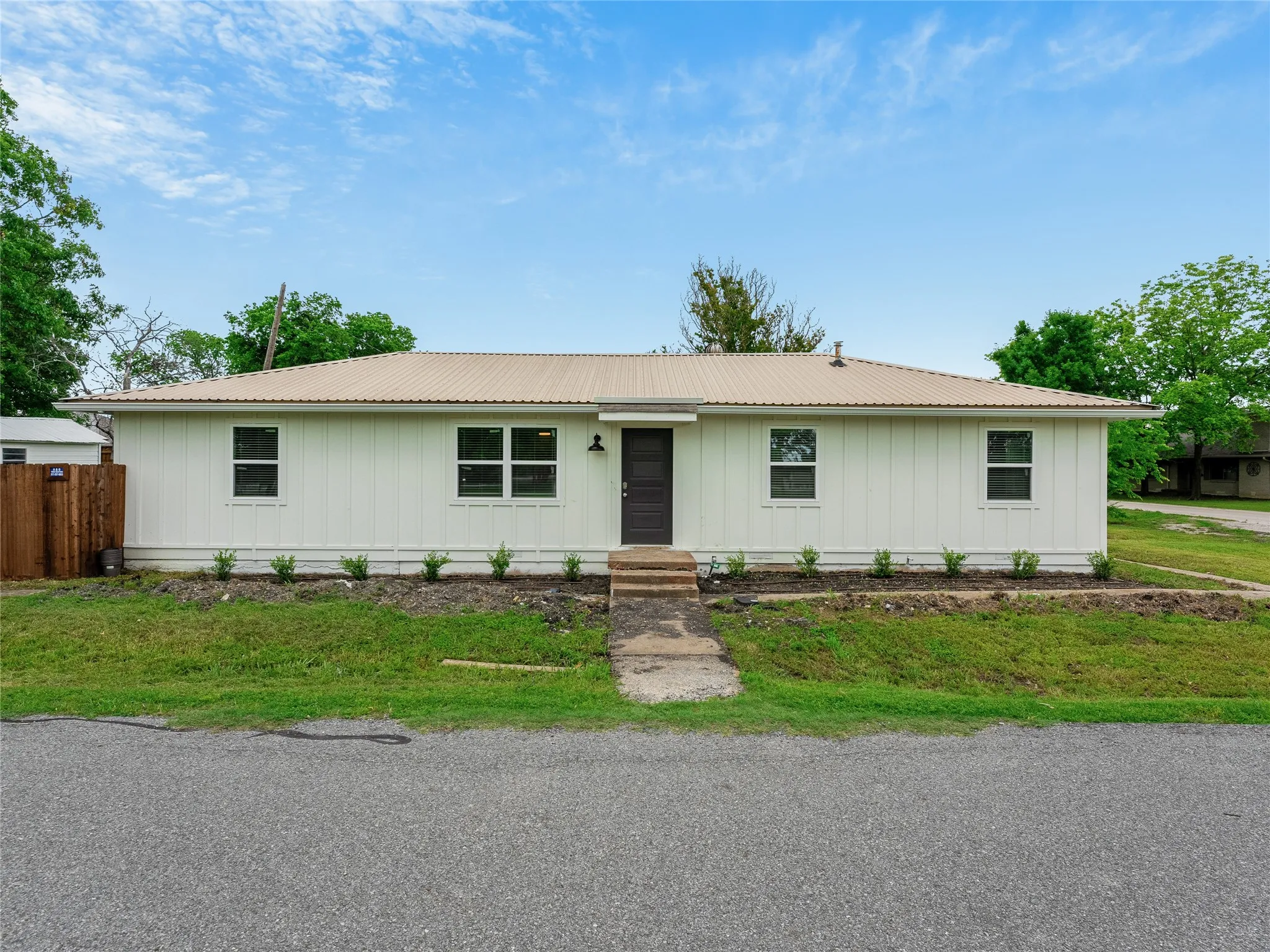 White vertical siding exterior, metal roof, dark entry door, multiple windows, front yard landscaping