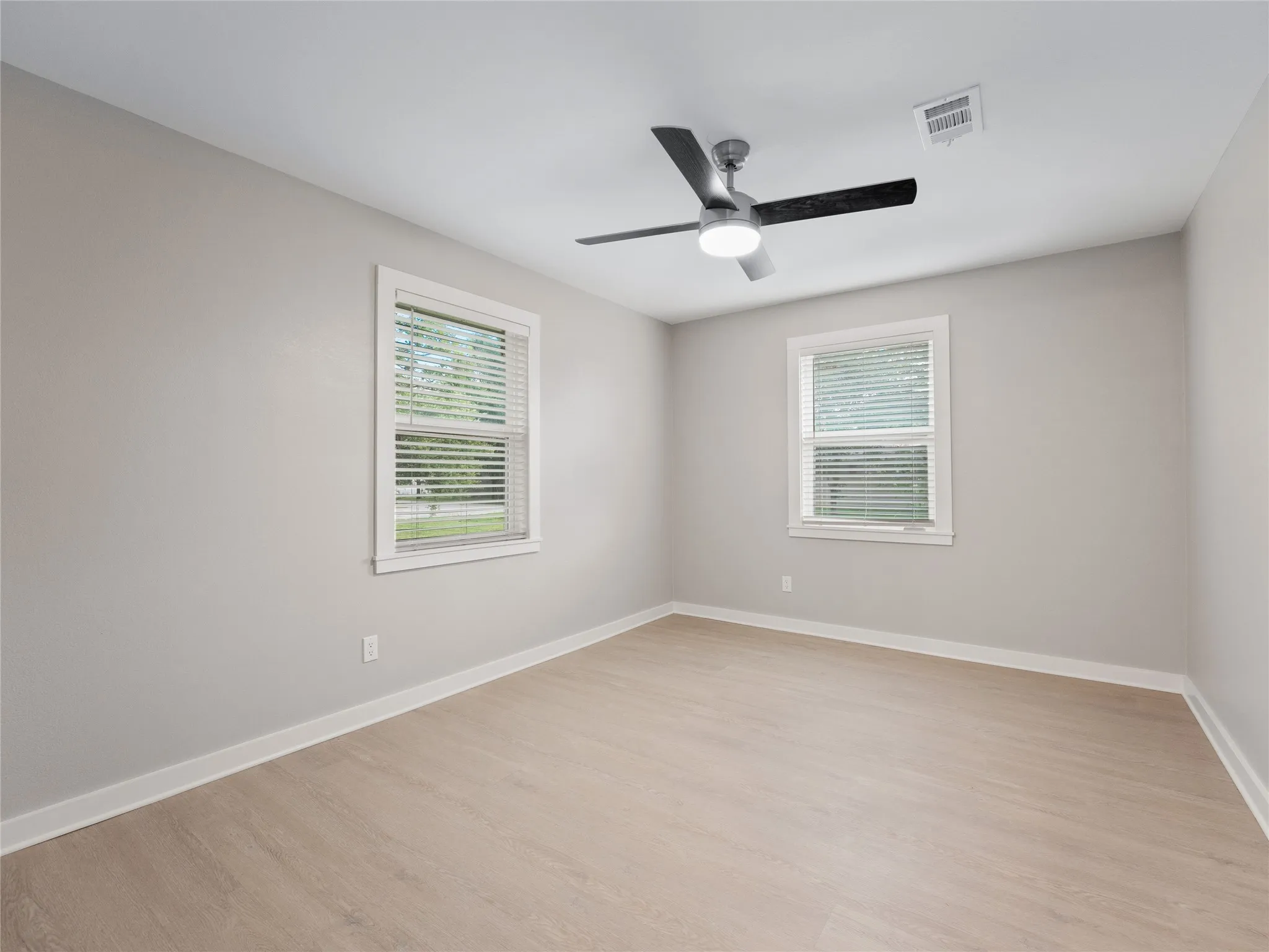 Room featuring two windows, a ceiling fan with integrated lighting, wood-finish flooring, and light-toned wall paint