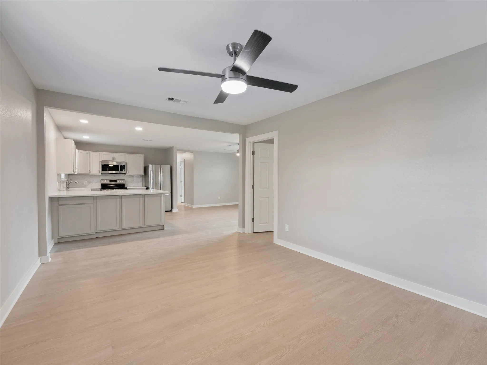 Light wood-finish flooring with a modern ceiling fan and recessed lighting