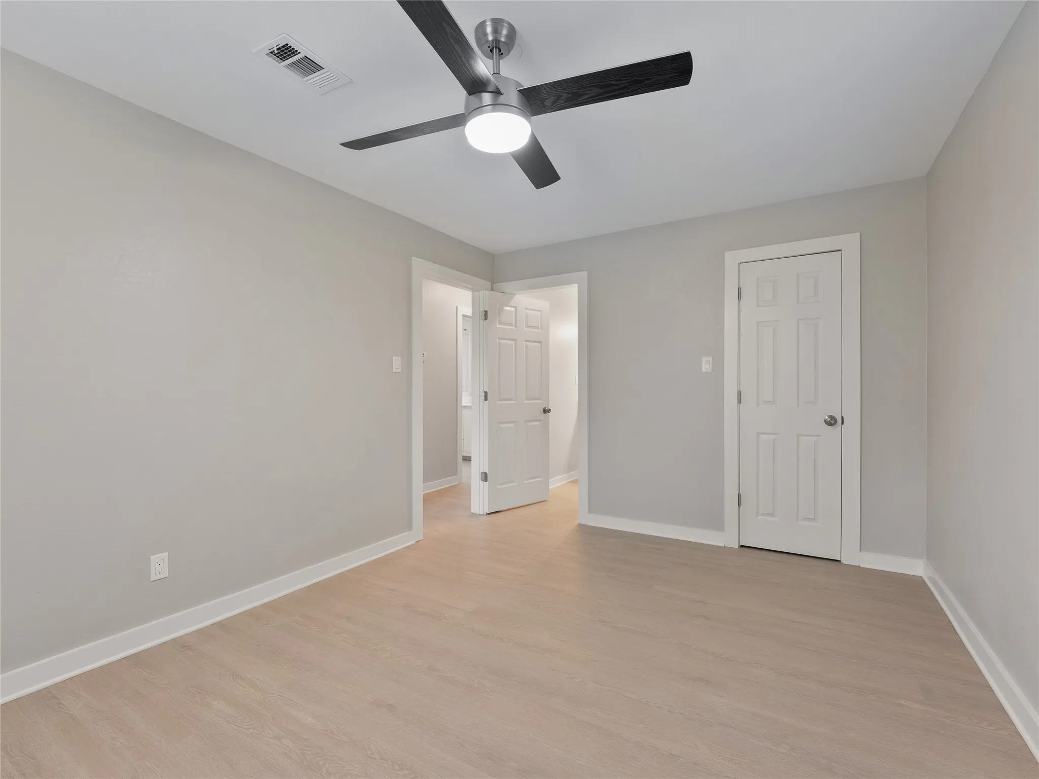 Light wood-finish flooring with white trim, a modern ceiling fan with light, and white paneled doors