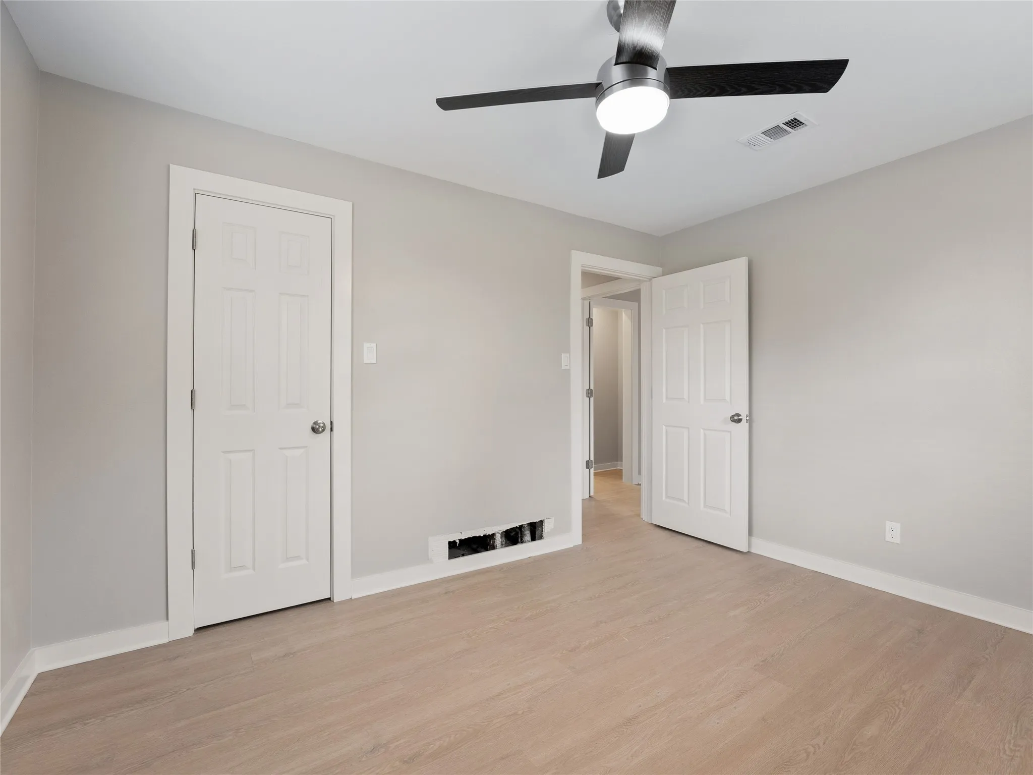 Light wood-finish flooring, neutral wall paint, and a modern ceiling fan with integrated lighting