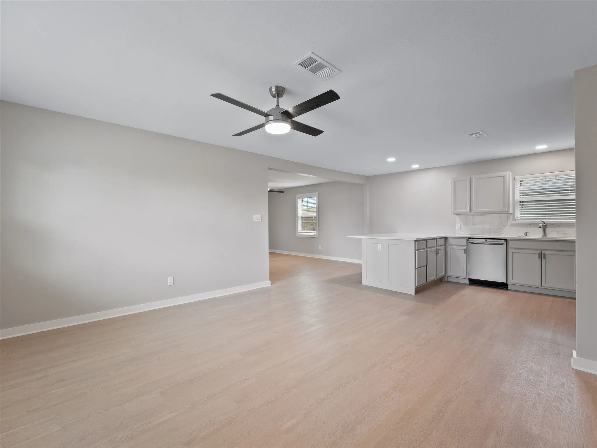 Open-concept living space featuring wood-finish flooring, a contemporary ceiling fan, recessed lighting, and a kitchen island with light-toned cabinetry and stainless steel appliances