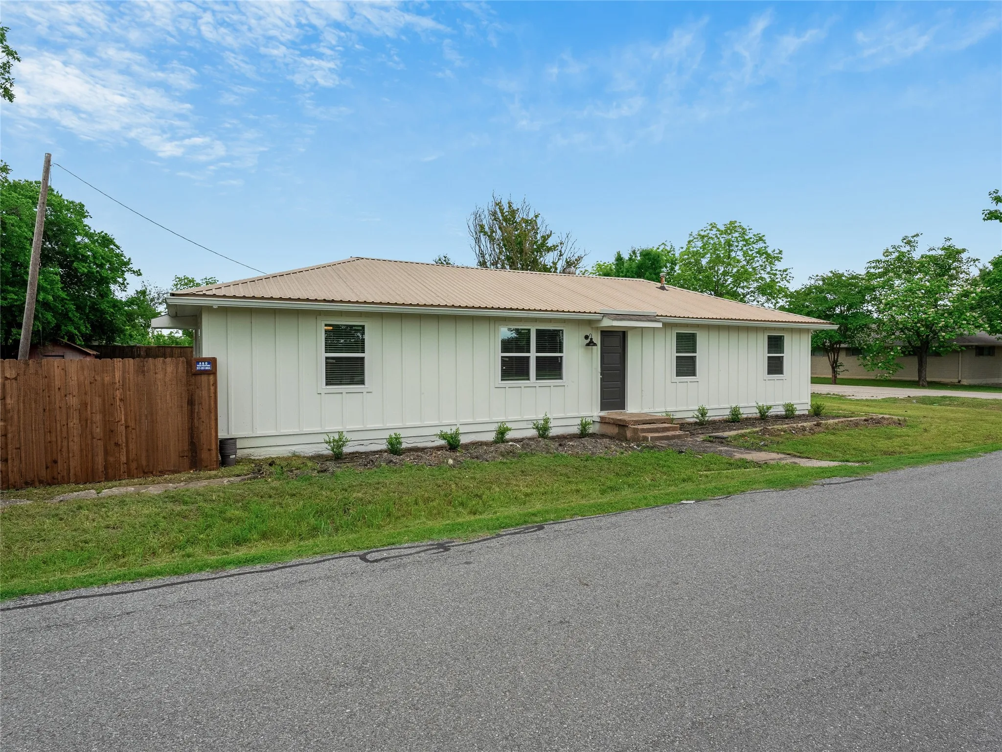 White board and batten exterior, metal roof, dark entry door, front landscaping with shrubs, and a wood privacy fence