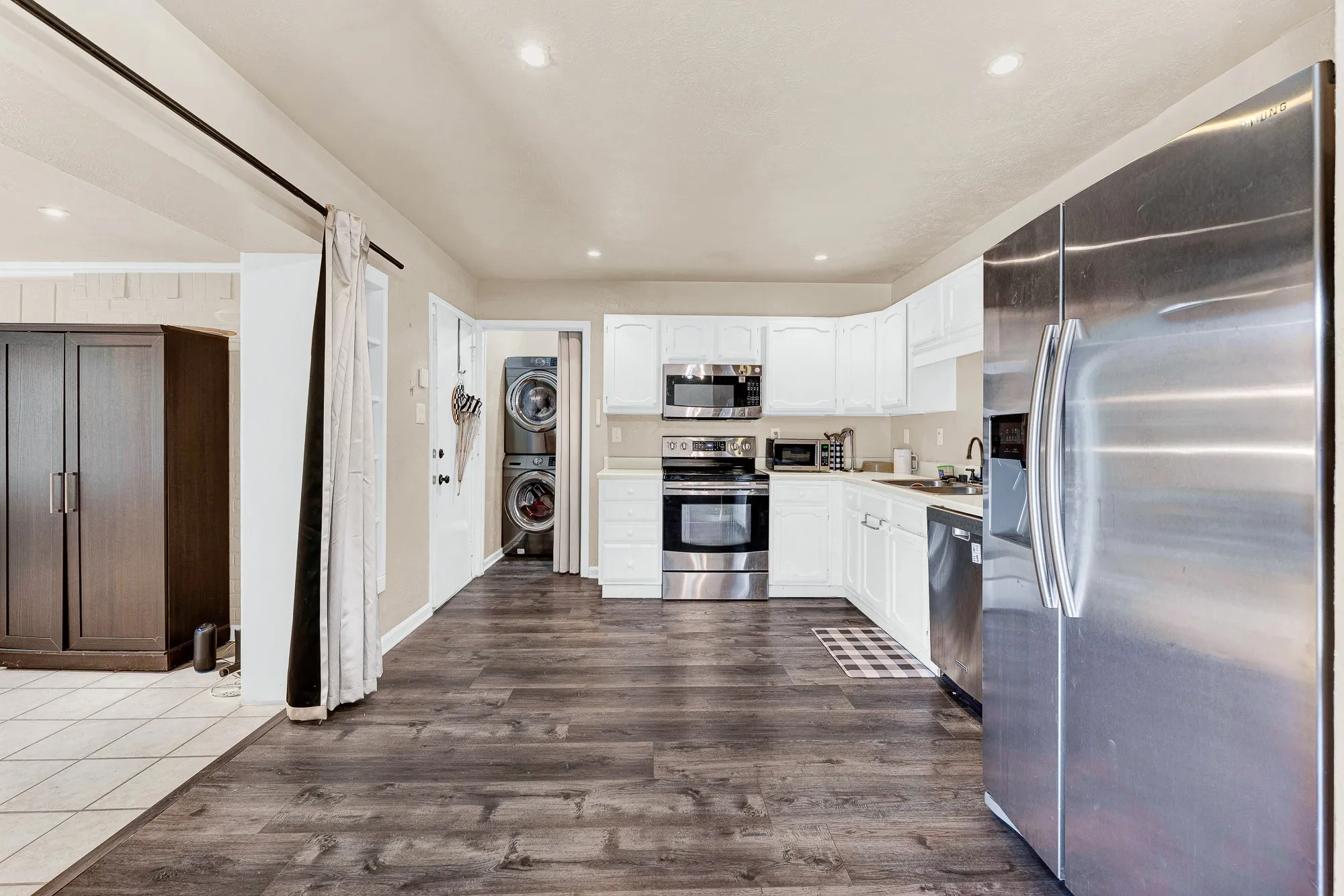 Wood-finish flooring, white cabinetry, stainless steel appliances, recessed lighting, and a stacked washer/dryer