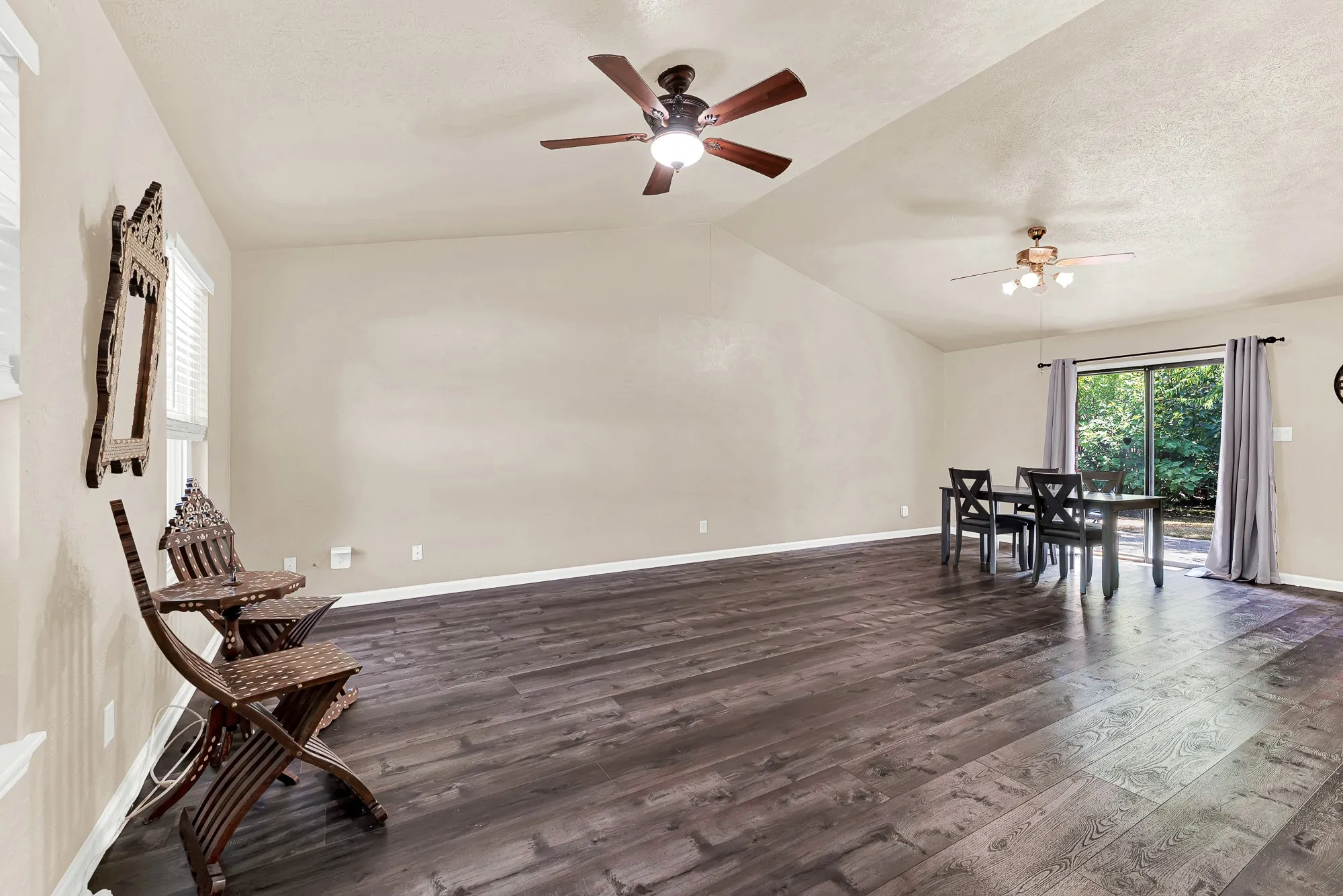 Vaulted ceiling with dual ceiling fans, wood-finish flooring, and sliding glass door access to the outdoors