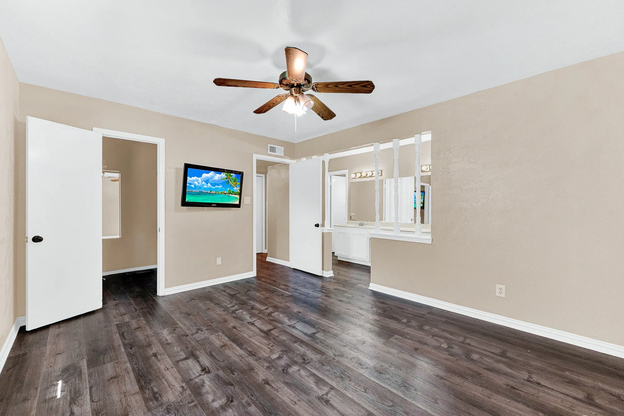 Wood-finish flooring, ceiling fan with light fixture, wall-mounted television, and a half-wall with decorative dividers