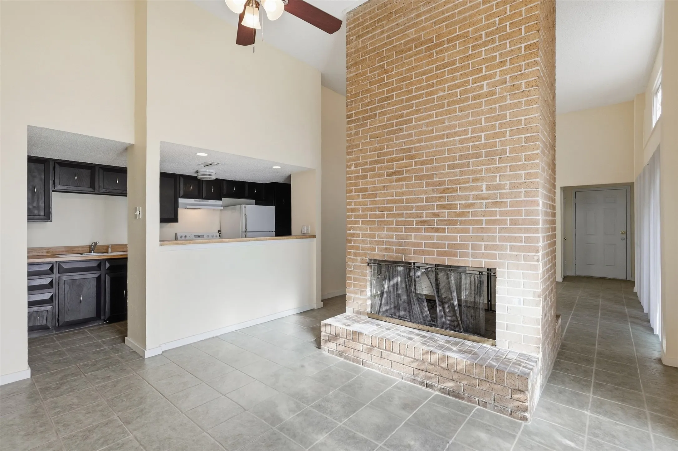 Vaulted ceiling, ceiling fan, brick fireplace, tile flooring, and a pass-through kitchen