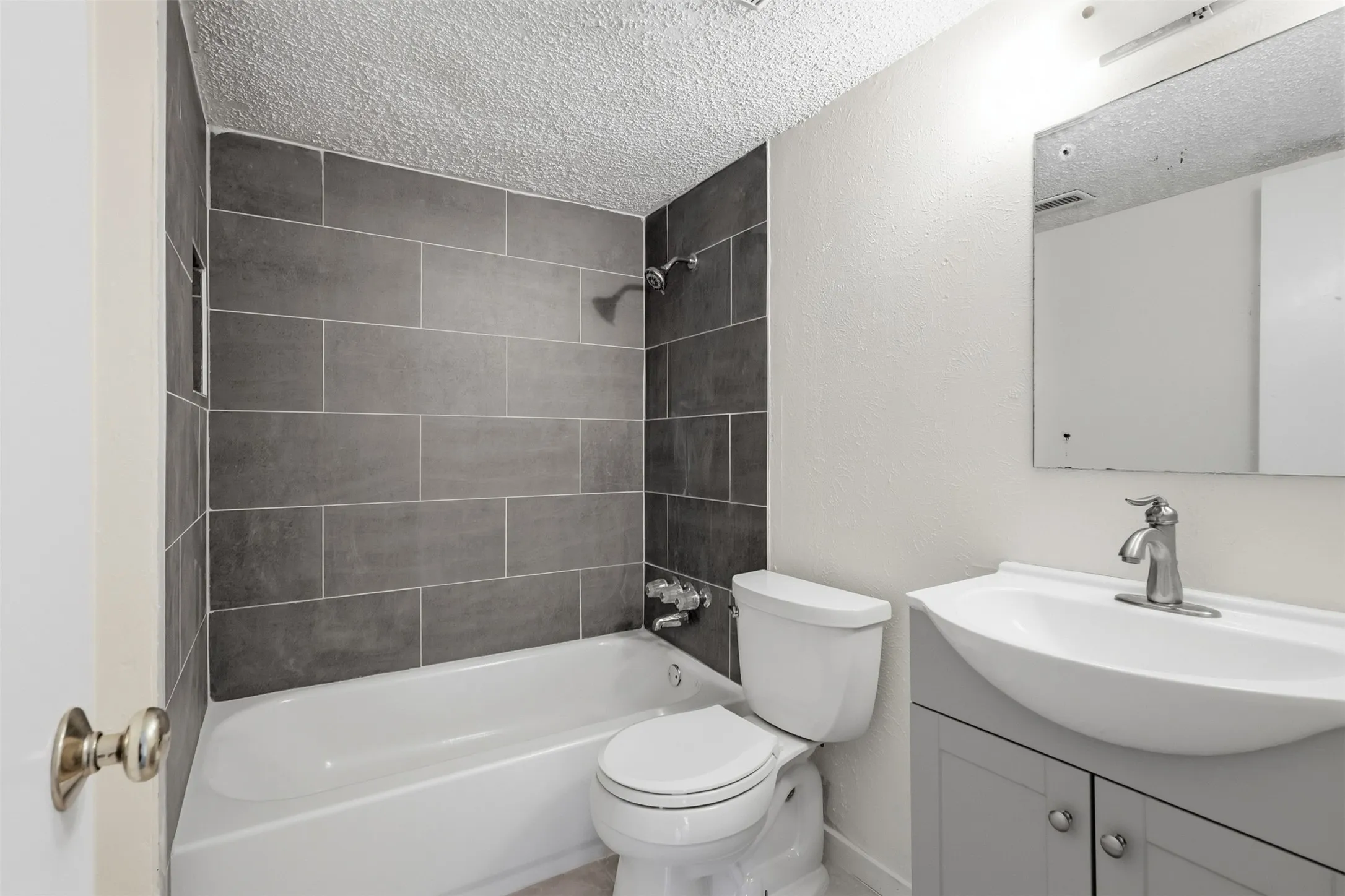 White bathtub and toilet with a gray tiled shower surround, recessed shower niche, and a vanity with an integrated sink