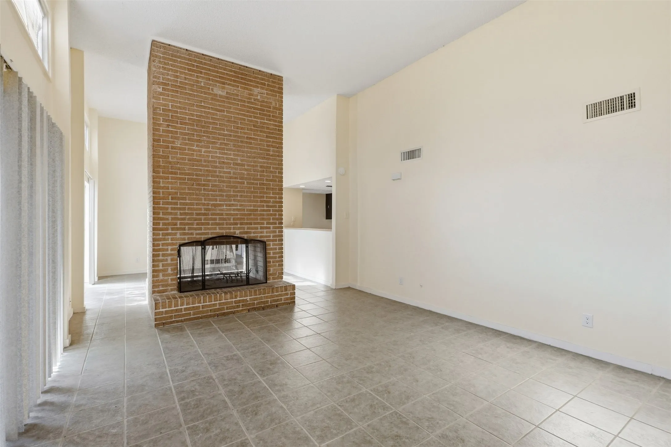 Brick fireplace with an arched firebox, tile flooring, and vaulted ceiling