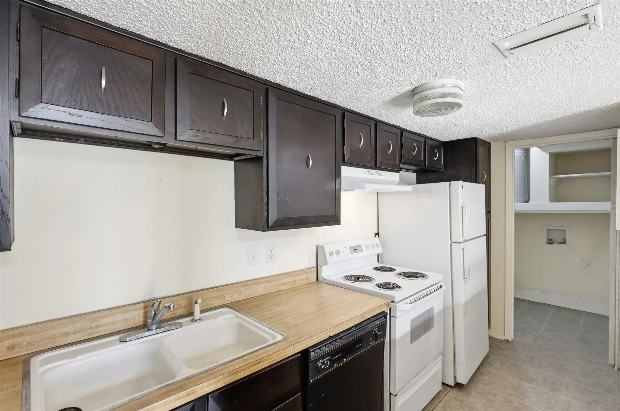 Kitchen featuring dark wood-finish cabinetry, white dual-basin sink, and a built-in dishwasher