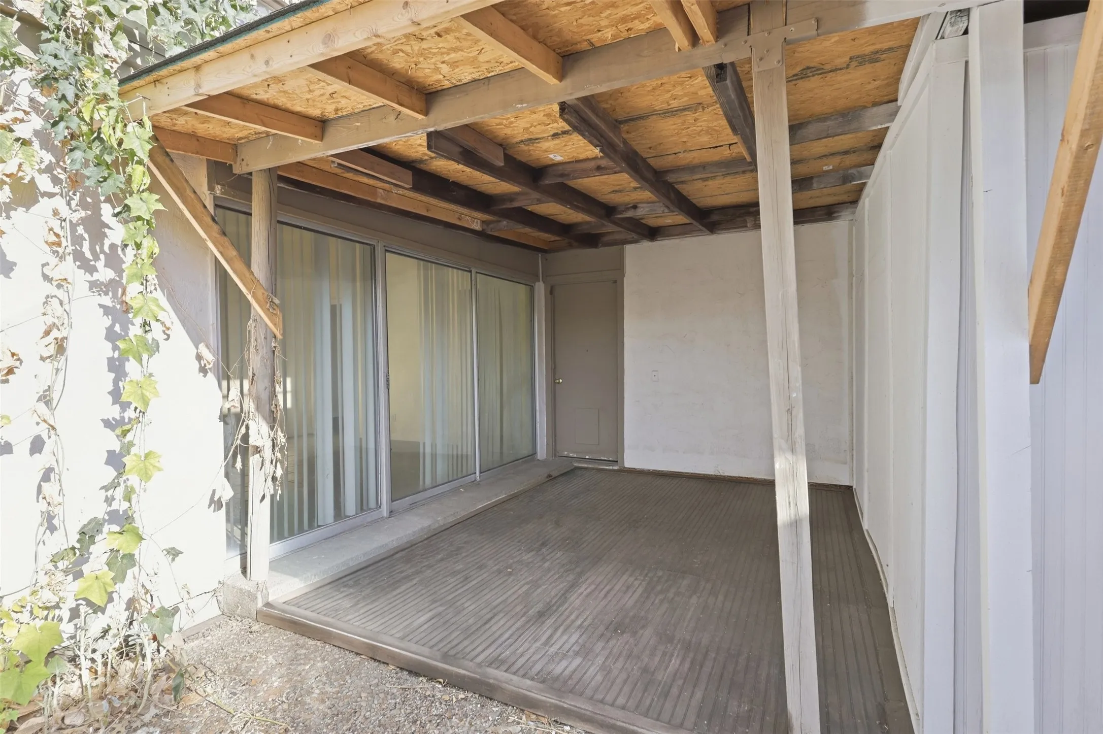 Covered outdoor patio featuring a wood-beam ceiling, concrete flooring, and an exterior door