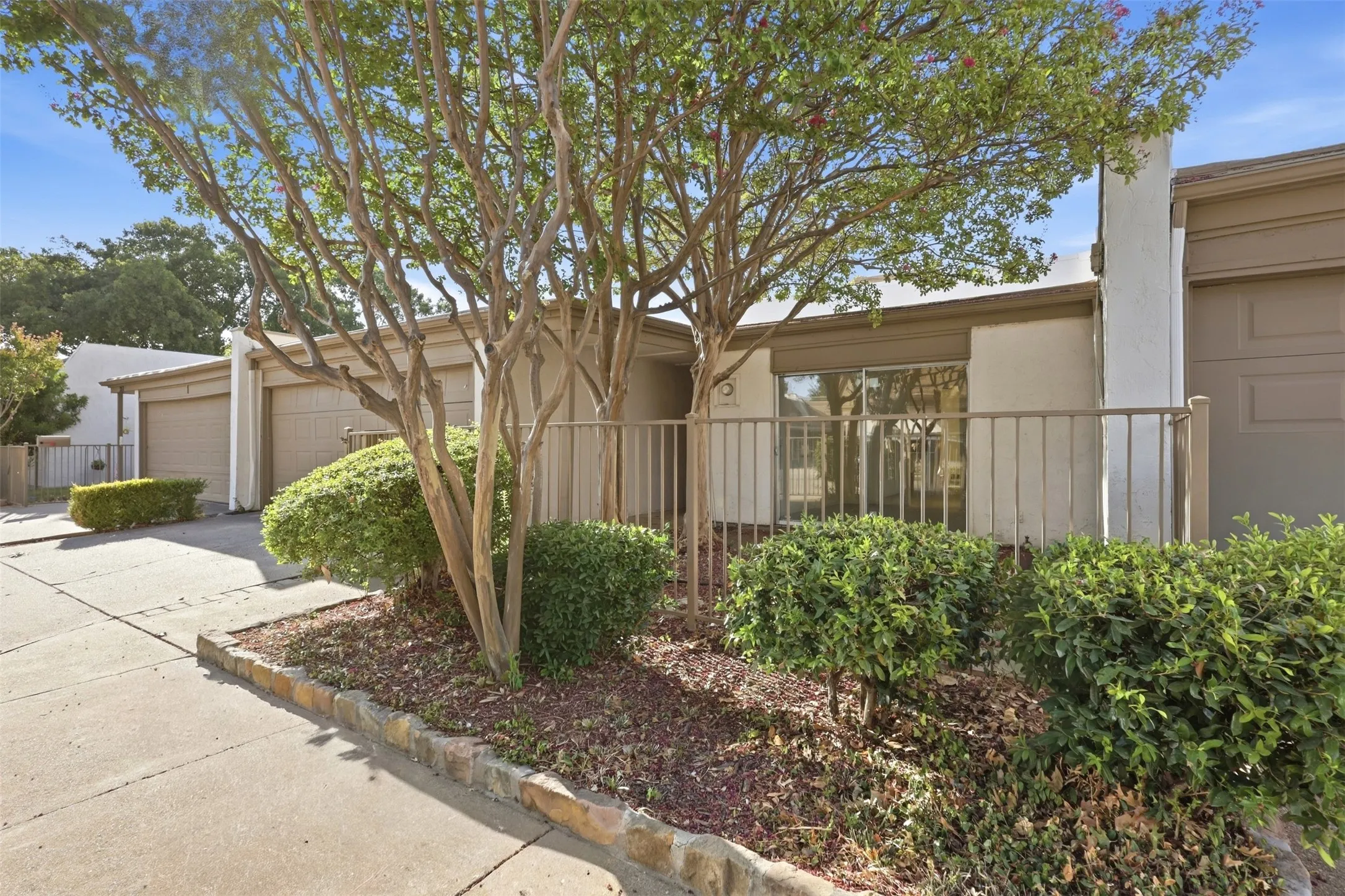 Stucco exterior with an attached garage, featuring a metal perimeter fence