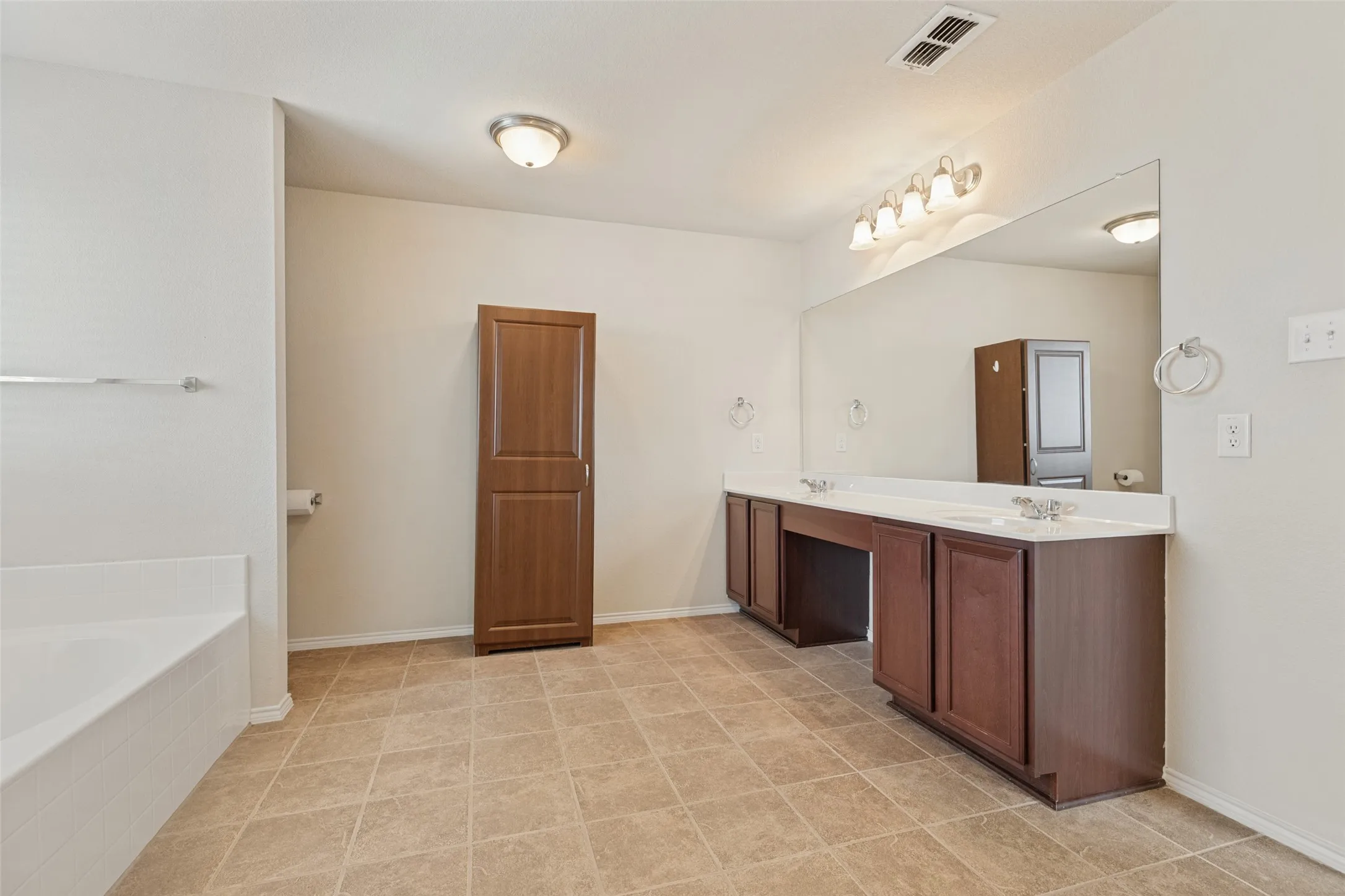Dual vanity with undermount sinks and white countertops, large wall-mounted mirror, wood-finish cabinetry, built-in storage cabinet, and tiled flooring