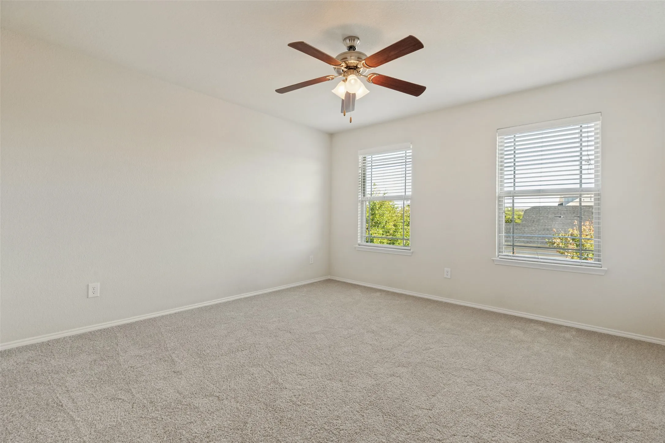 Neutral tone wall paint, carpeted flooring, two windows with blinds, and a ceiling fan with integrated lighting