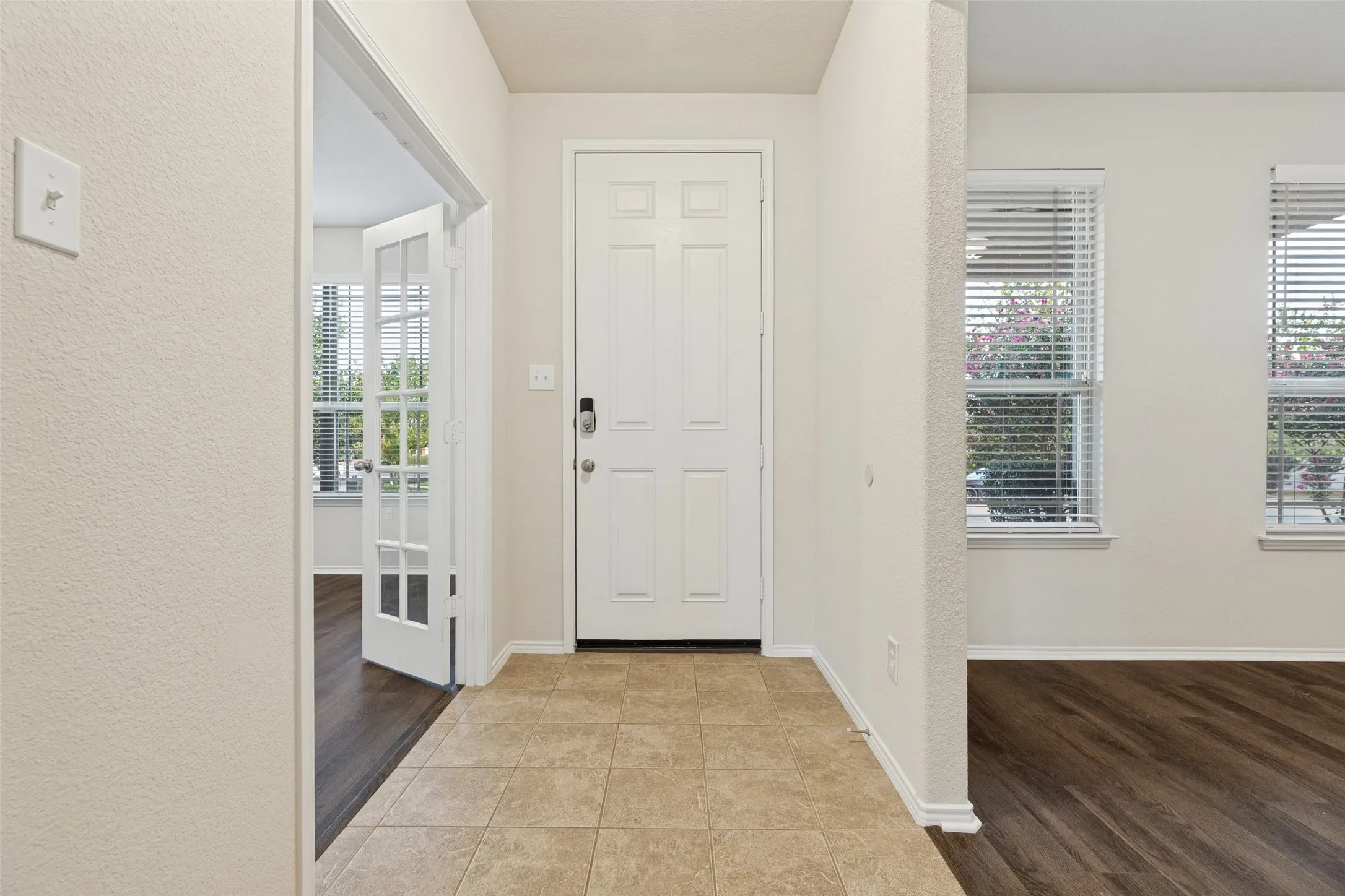Entryway featuring tiled flooring, a paneled door, and adjacent room with wood-finish flooring and French doors