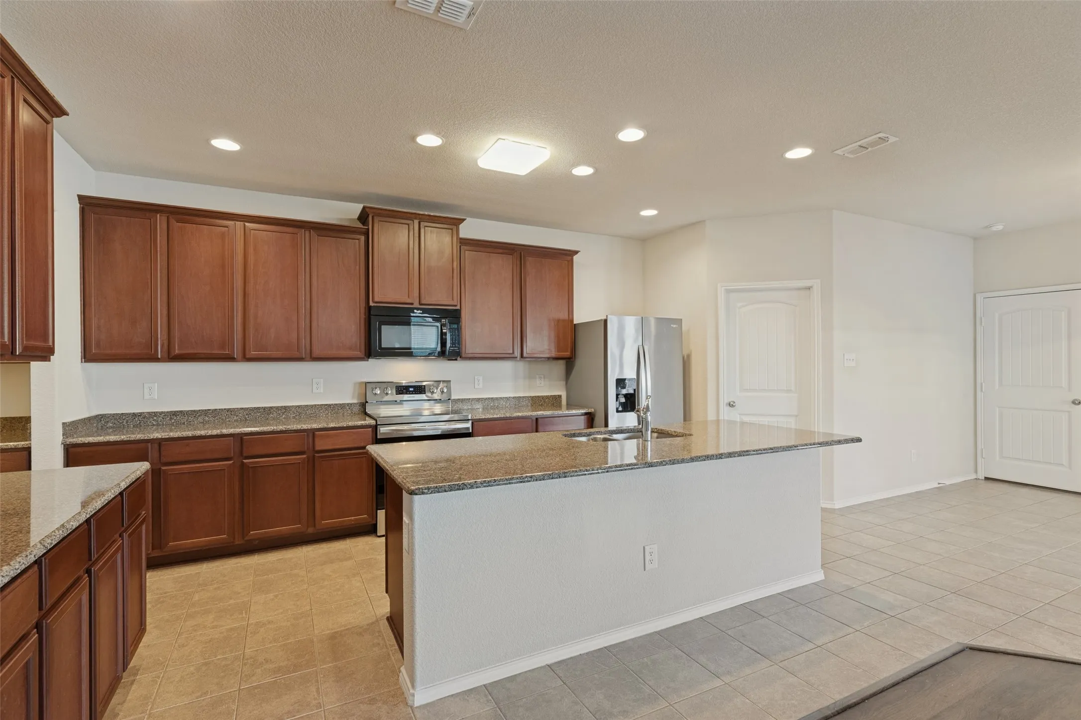 Kitchen featuring wood cabinetry, granite countertops, a central island with an undermount sink, stainless steel appliances, and recessed lighting