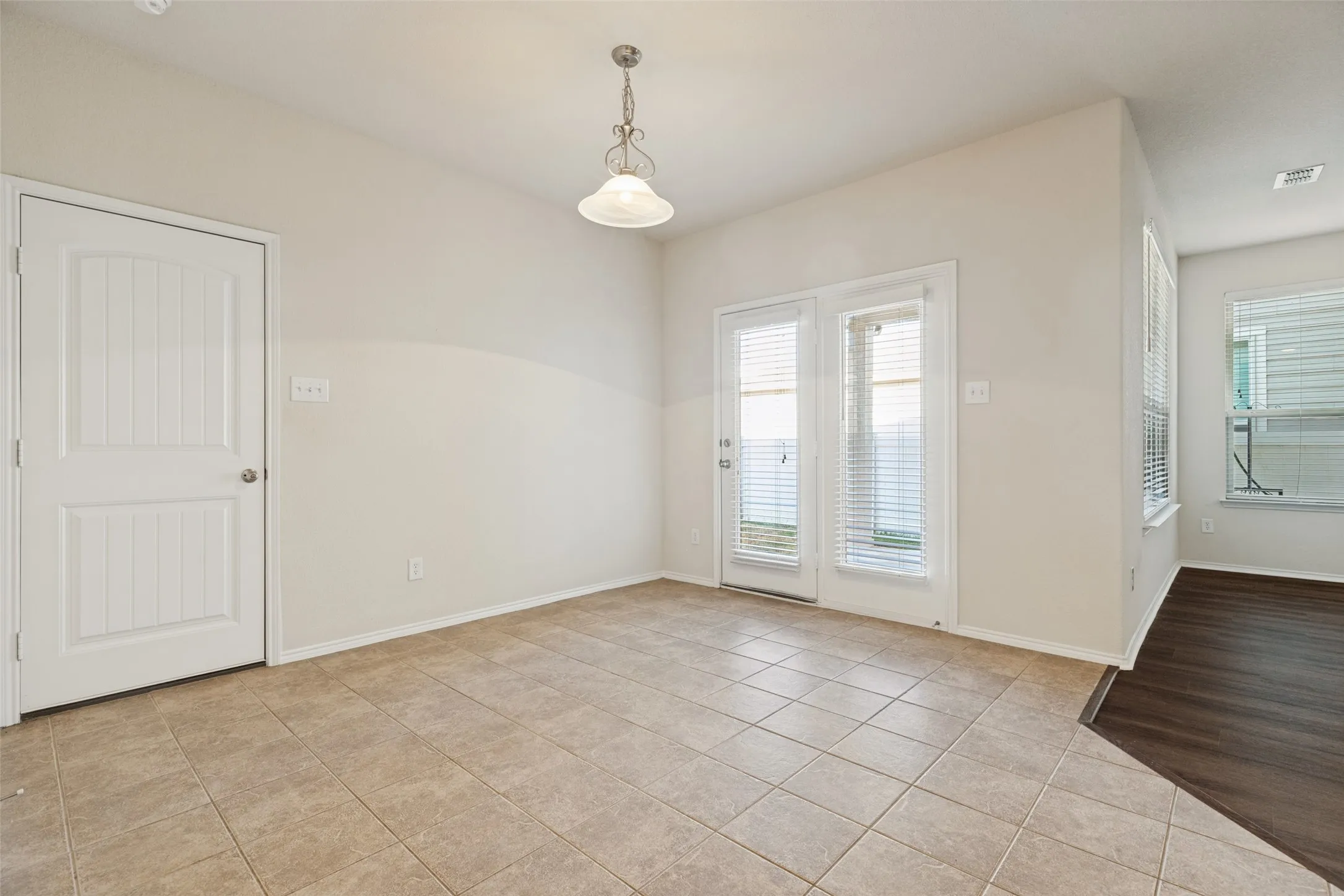 Neutral-toned ceramic tile flooring, white interior door with vertical paneling, double French doors, and a decorative pendant light fixture