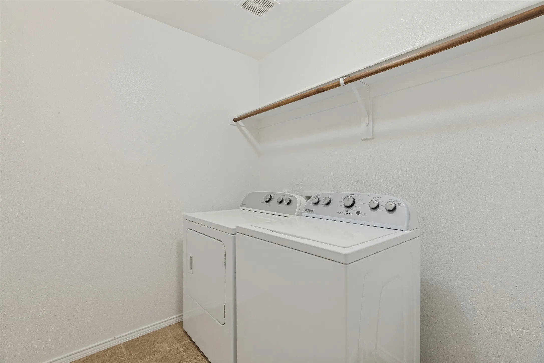 Laundry area featuring a wood-finish hanging rod on white brackets and tile flooring