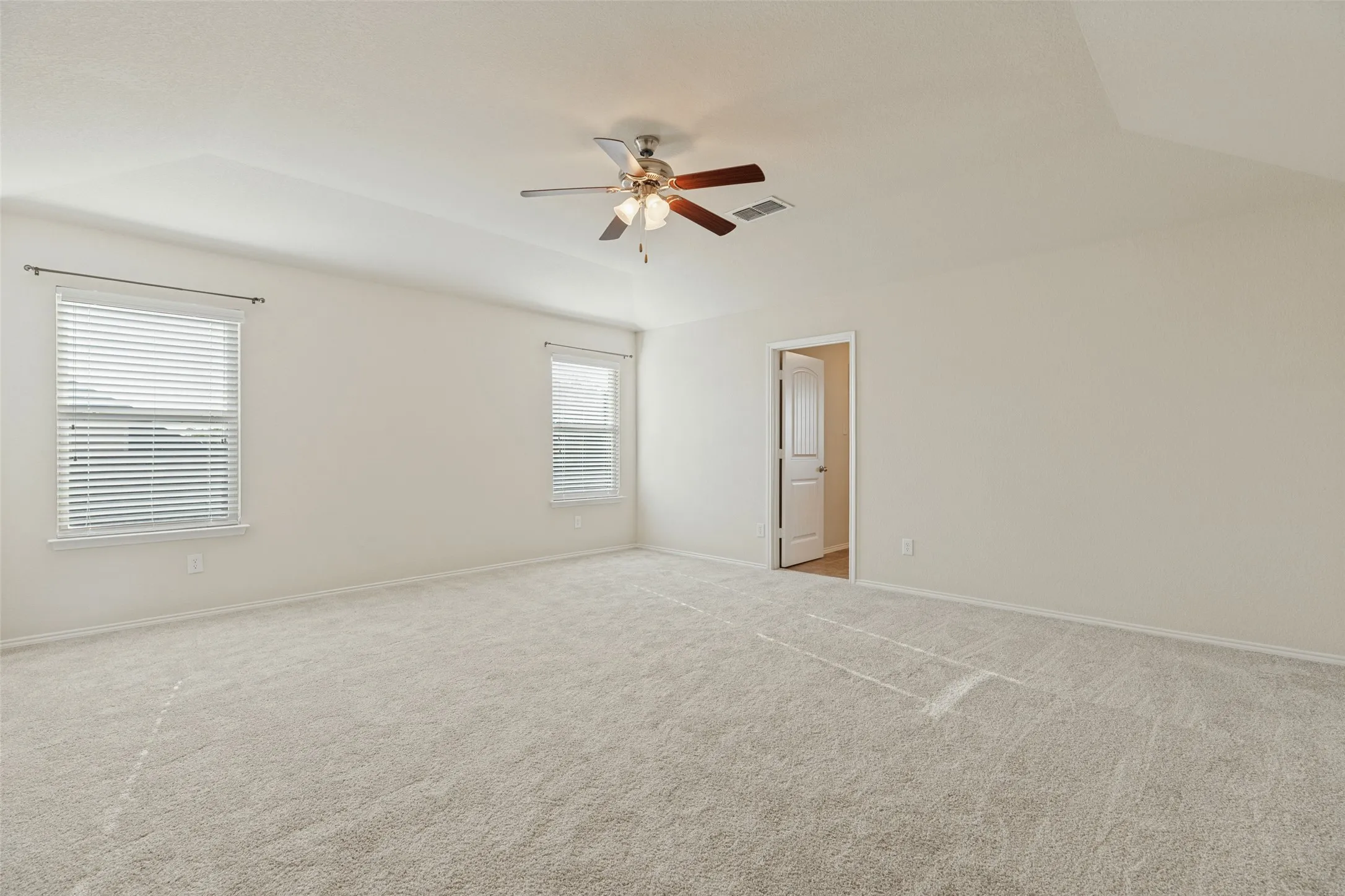 Expansive room featuring vaulted ceilings, light-toned carpeting, dual windows with blinds, and a ceiling fan with integrated lighting