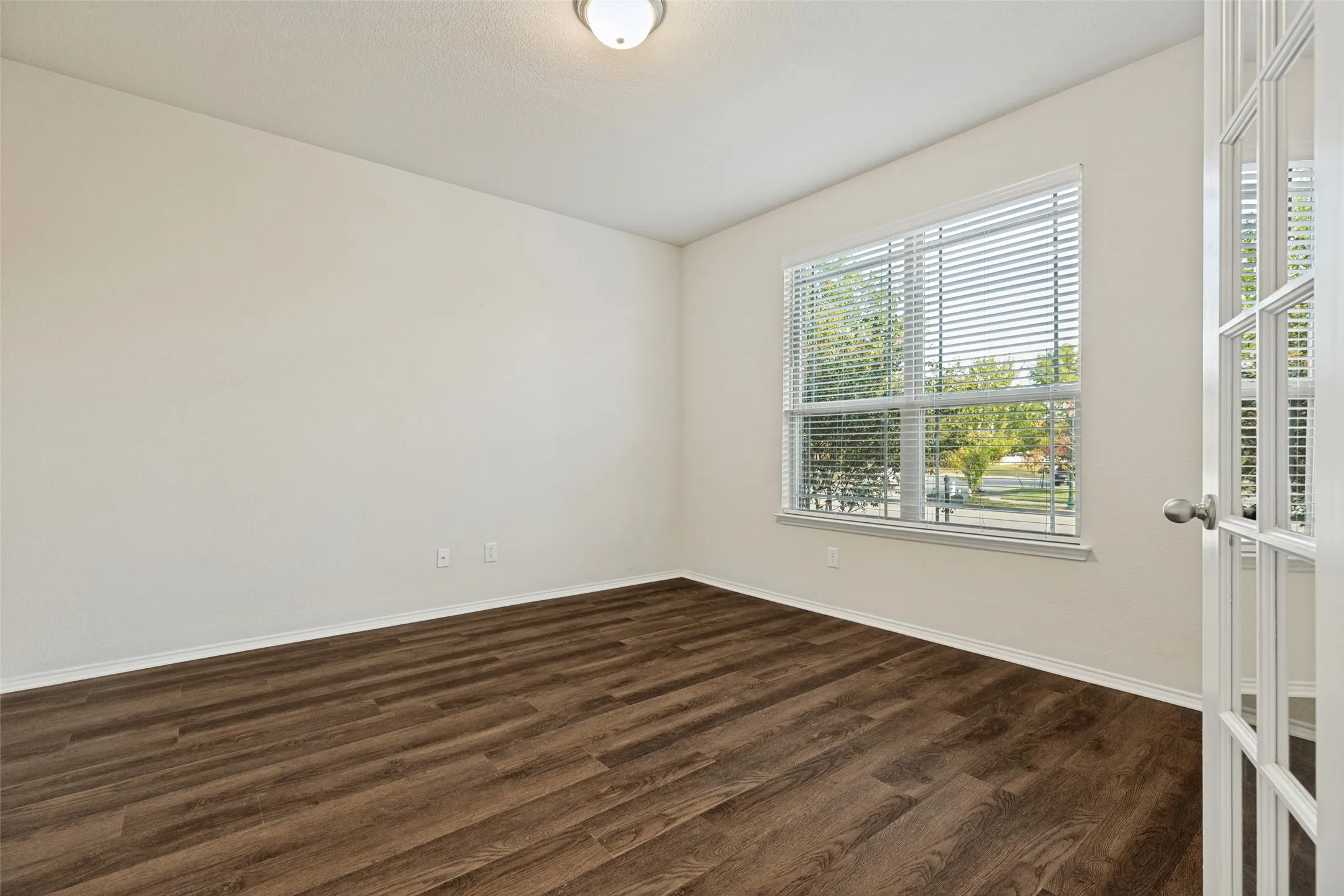 Wood-finish flooring, neutral wall tones, and a large window with blinds