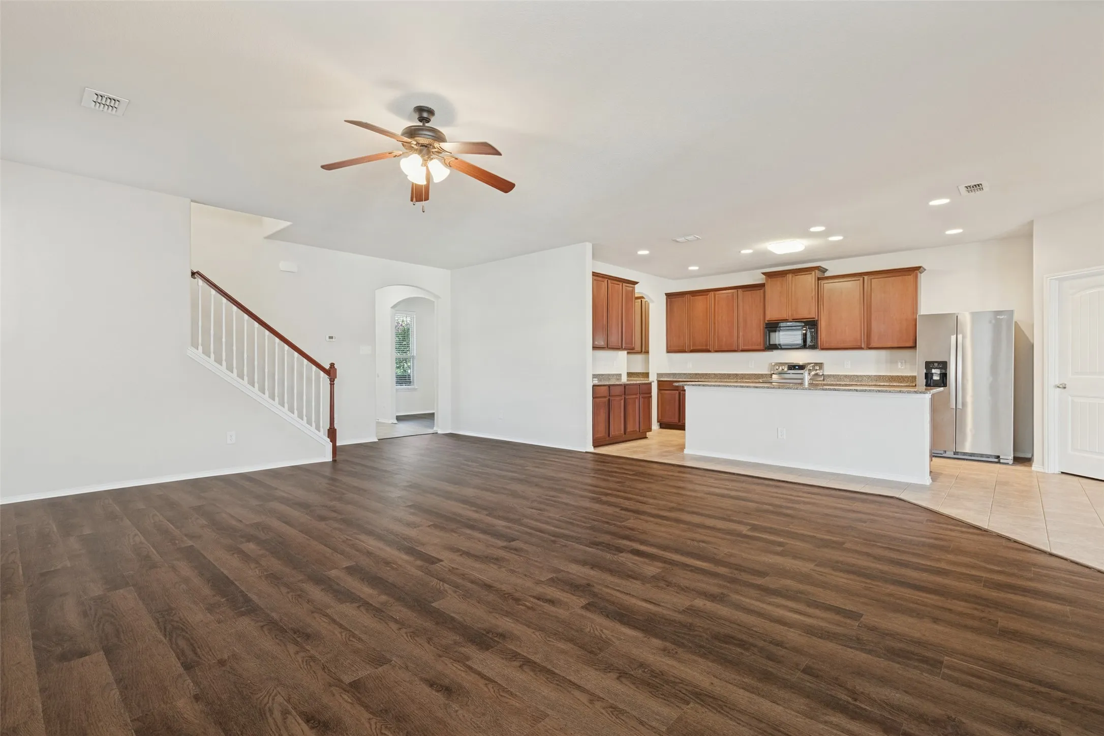 Open-concept living space featuring wood-finish flooring, a ceiling fan, and a staircase with white balusters and wood handrail