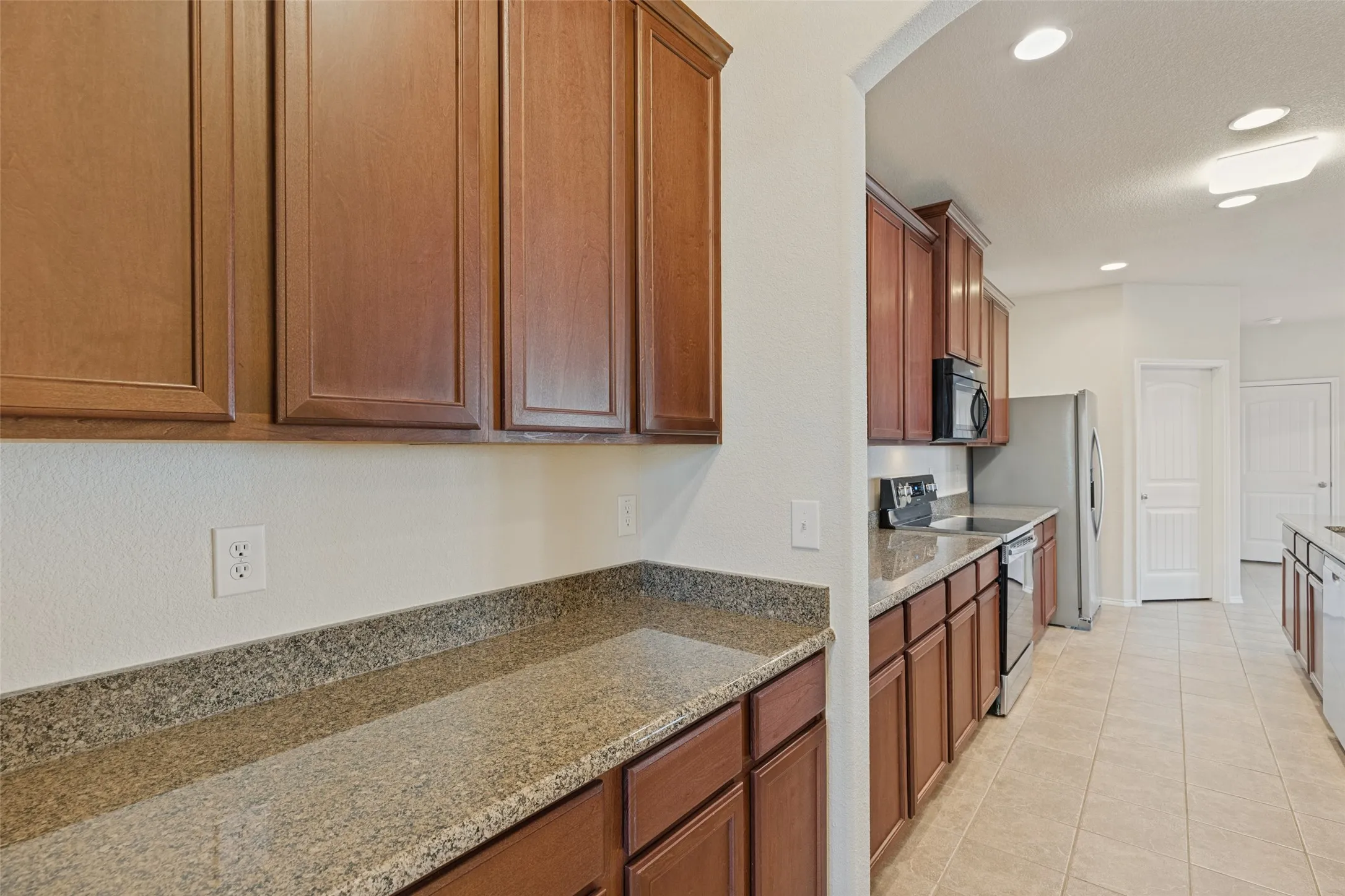 Kitchen featuring wood cabinetry, stone-look countertops, stainless steel appliances, and recessed lighting