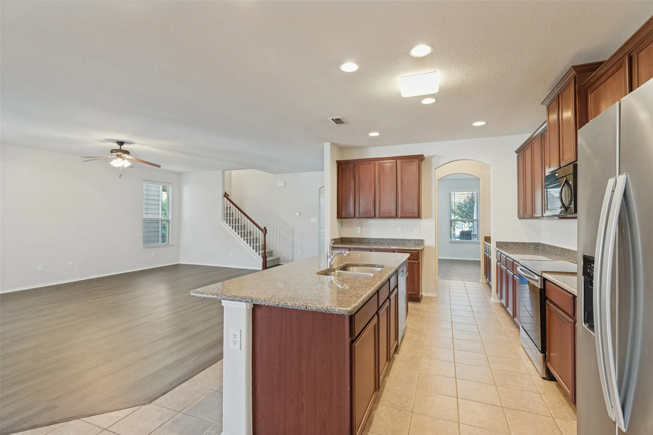 Kitchen island with integrated sink, stainless steel appliances, wood-finish cabinetry, tile flooring, and recessed lighting