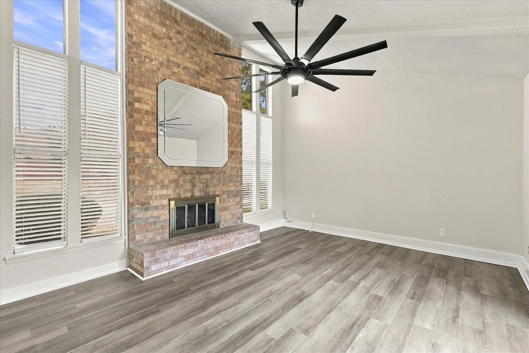 Brick fireplace with a hearth, wood-finish flooring, and a ceiling fan