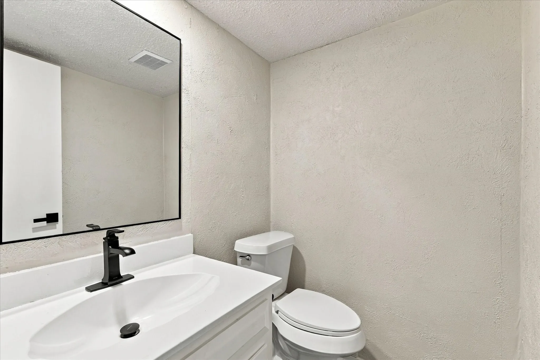 White vanity with a rectangular basin, matte black faucet, and frameless mirror