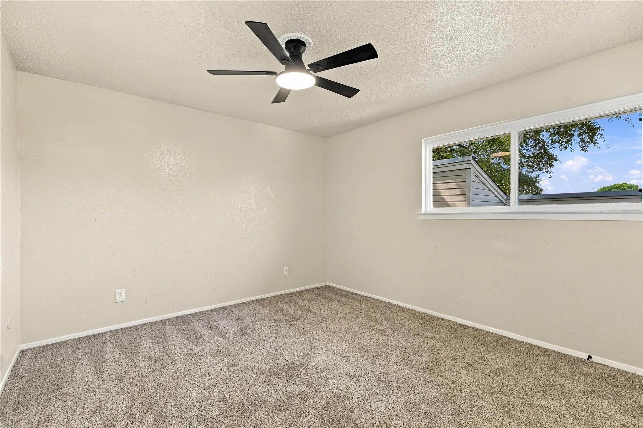 Textured walls, ceiling fan with integrated lighting, window with white trim, and carpeted flooring