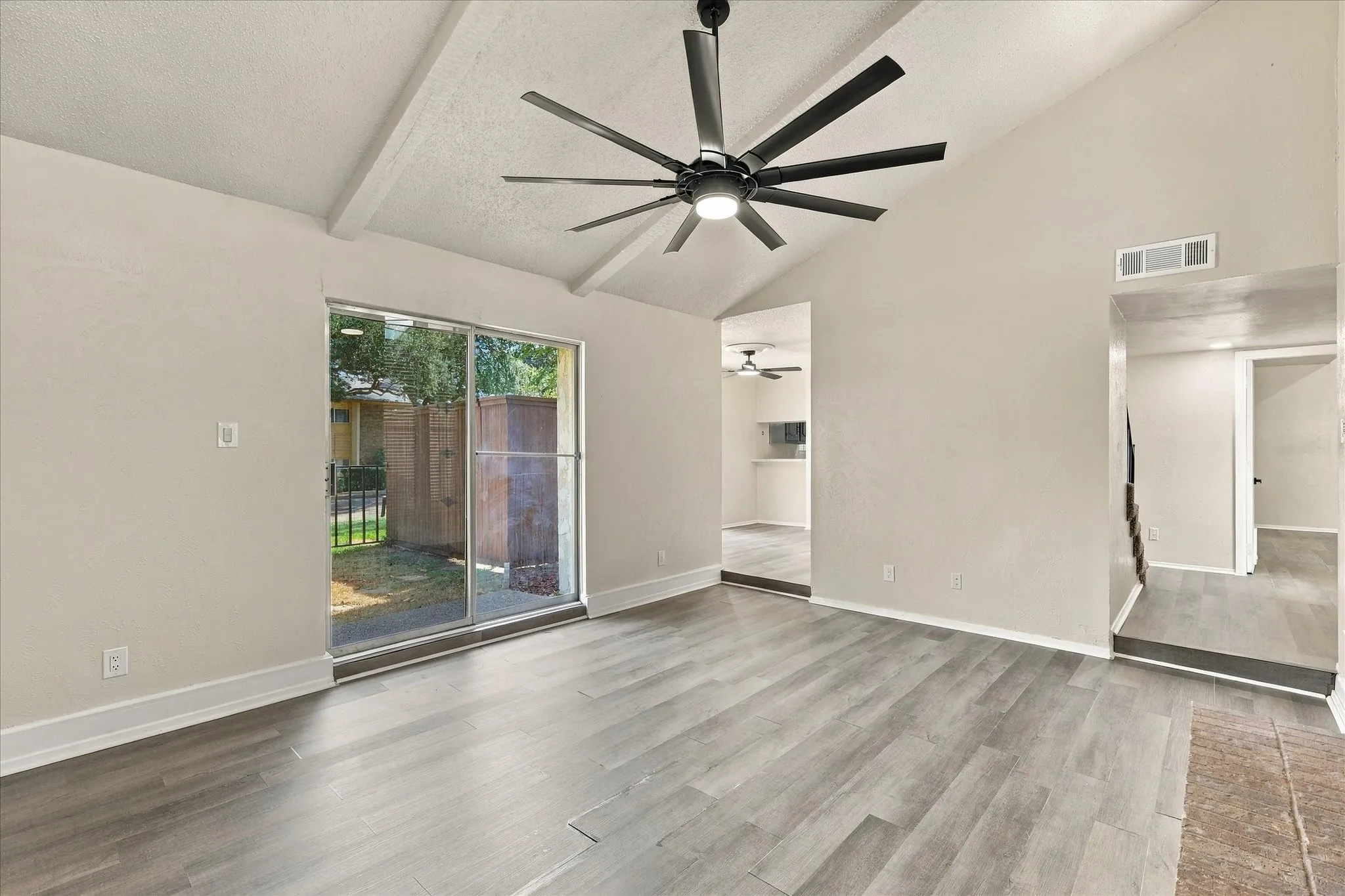 Vaulted ceilings with exposed beams, wood-finish flooring, and a contemporary ceiling fan