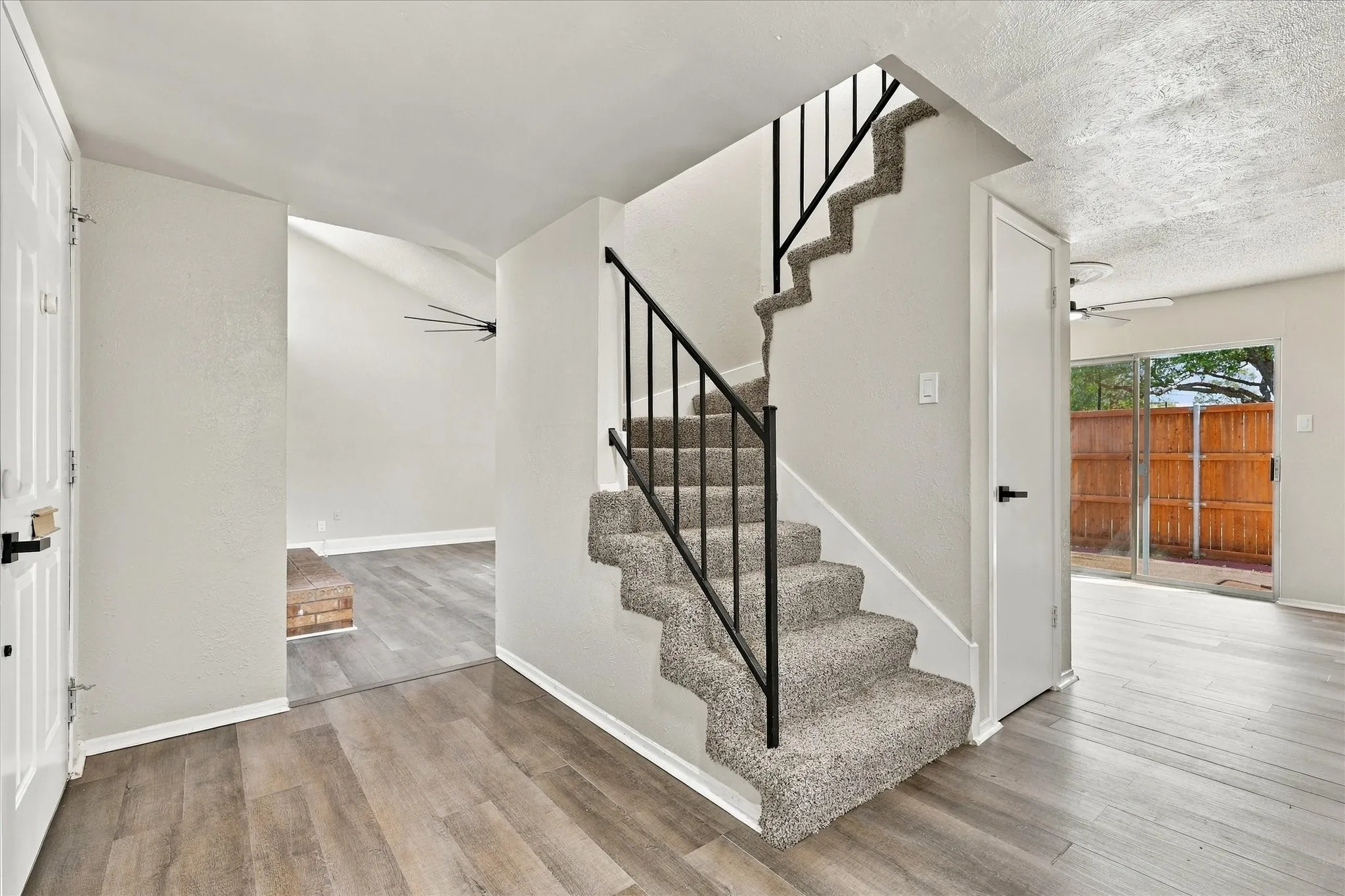 Wood-finish flooring, carpeted staircase with wrought iron railing, sliding glass door, and vaulted ceiling