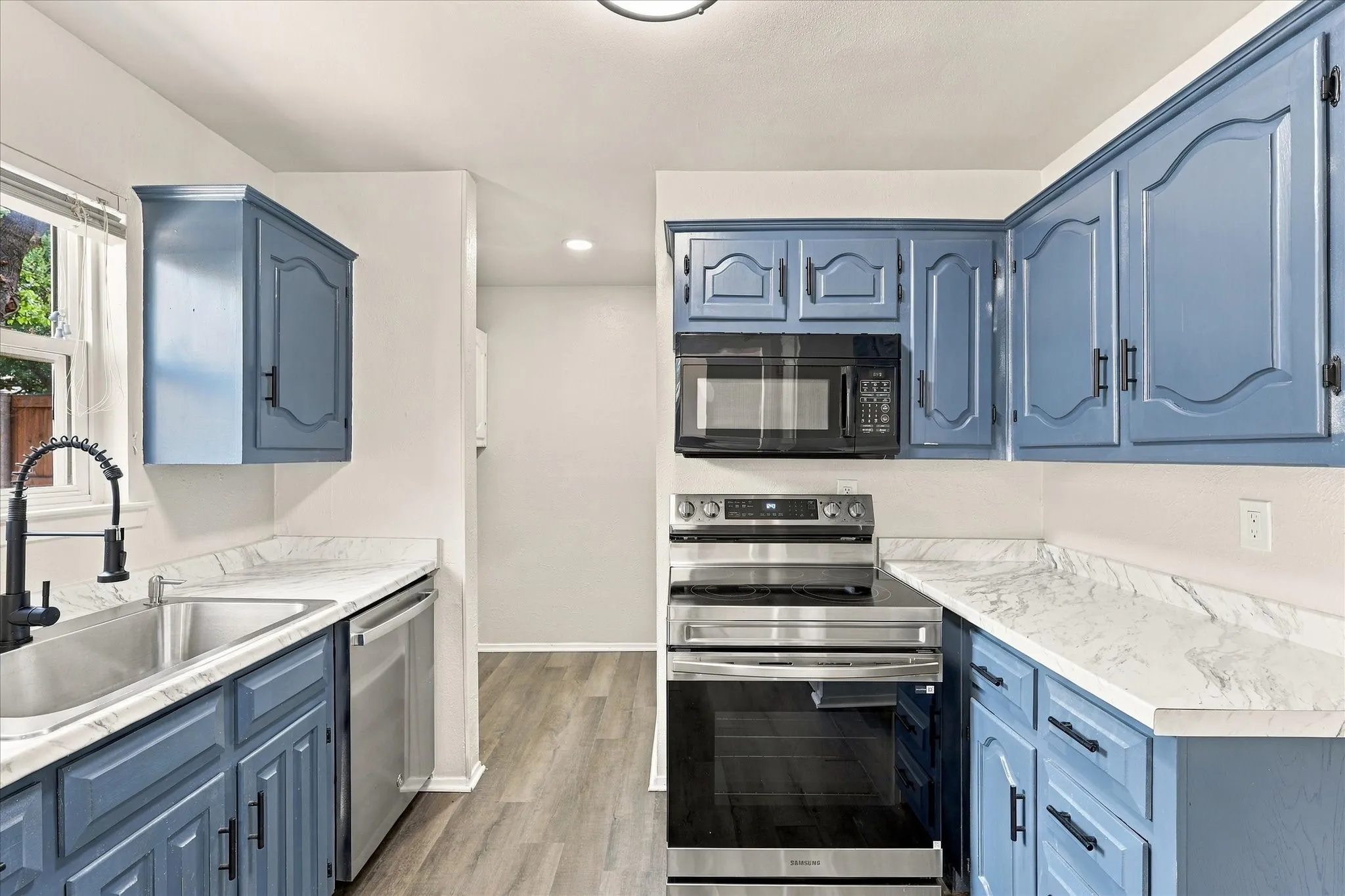 Kitchen with blue cabinetry, white countertops, stainless steel appliances, and wood-finish flooring