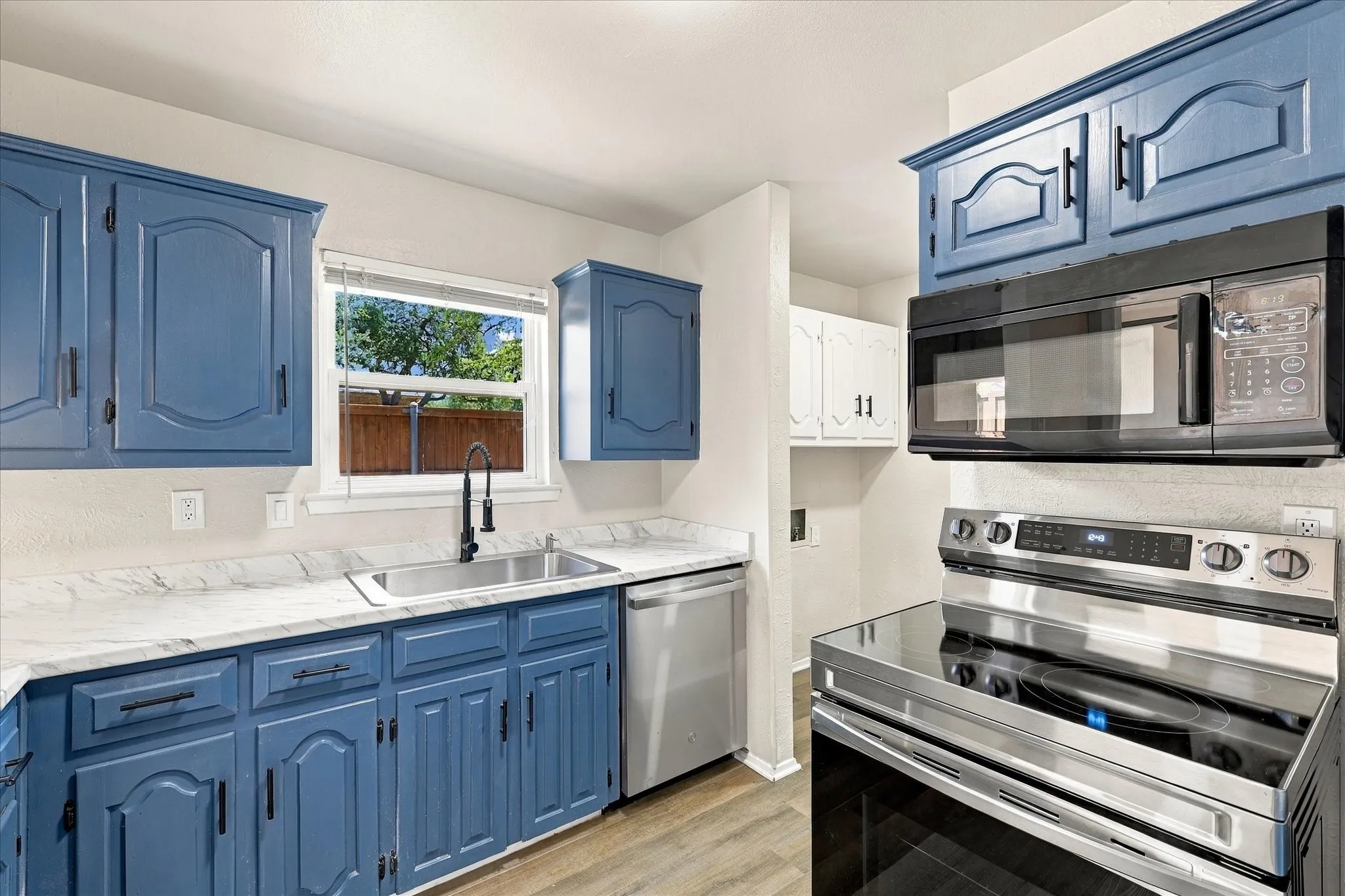 Kitchen featuring painted blue cabinetry, light-toned countertops, stainless steel sink with a matte black faucet, a stainless steel dishwasher, and a stainless steel range with an overhead microwave