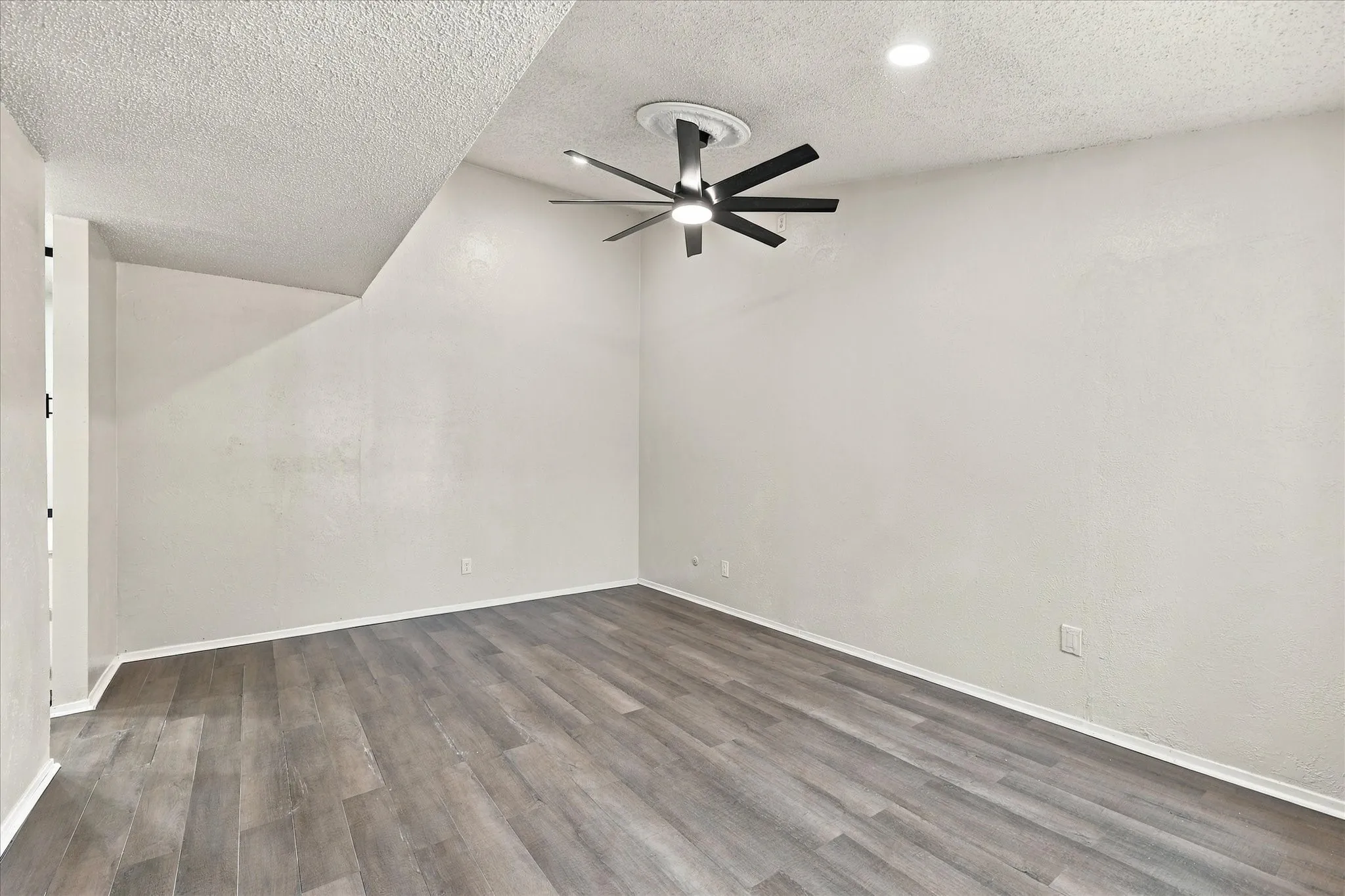 Wood-finish flooring with crisp white baseboards, featuring a modern ceiling fan and recessed lighting